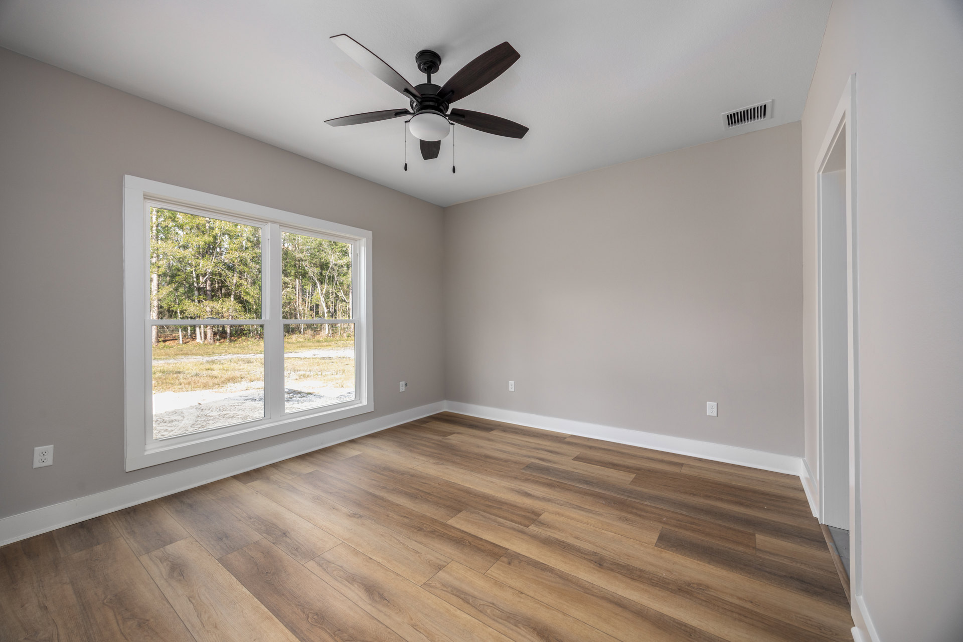 Ceiling fan with light fixture, wood flooring, large window overlooking trees, white plaster walls