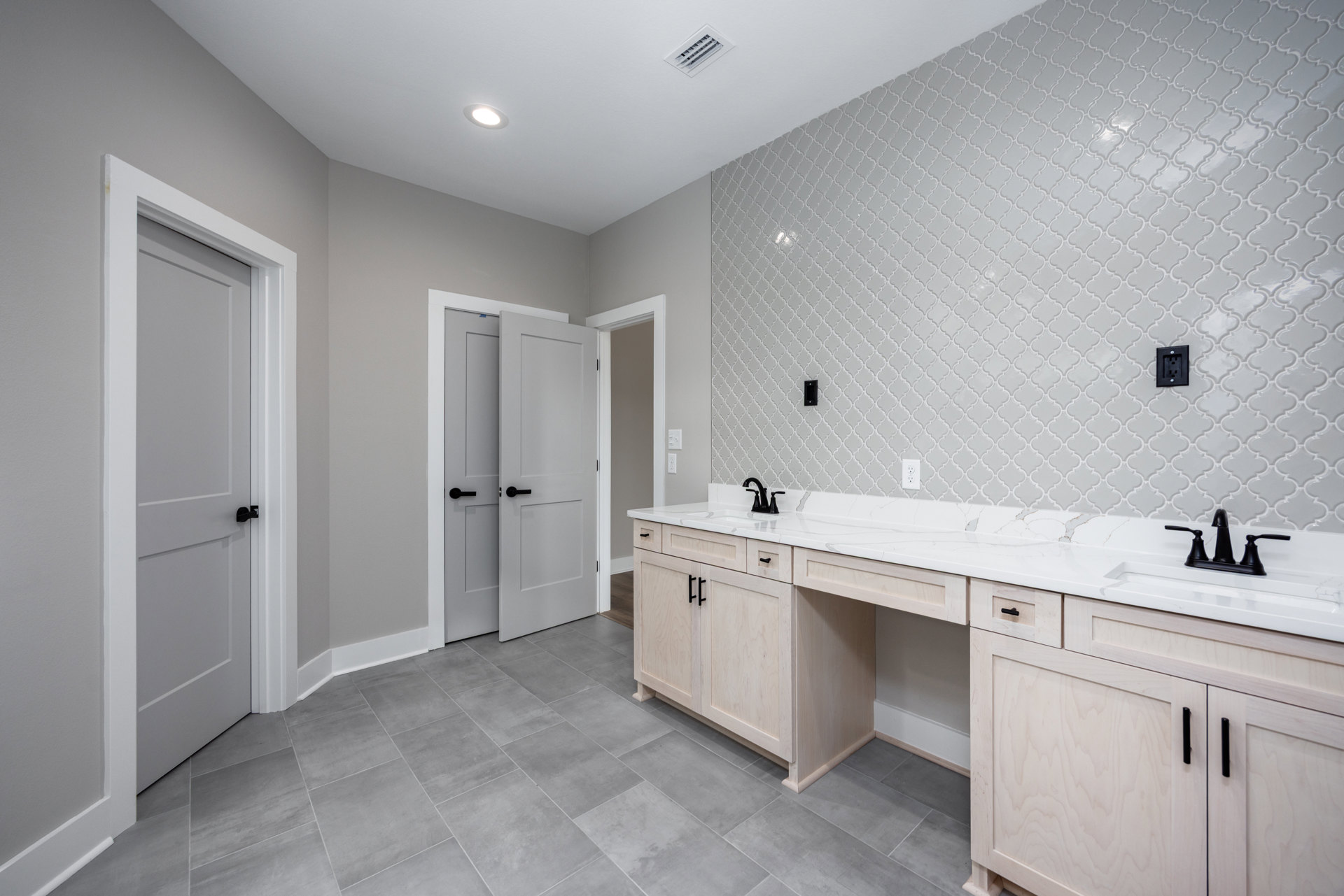 Bathroom with white tile wall, white cabinetry, black door handles, ceiling vent, and countertop sink with chrome faucet