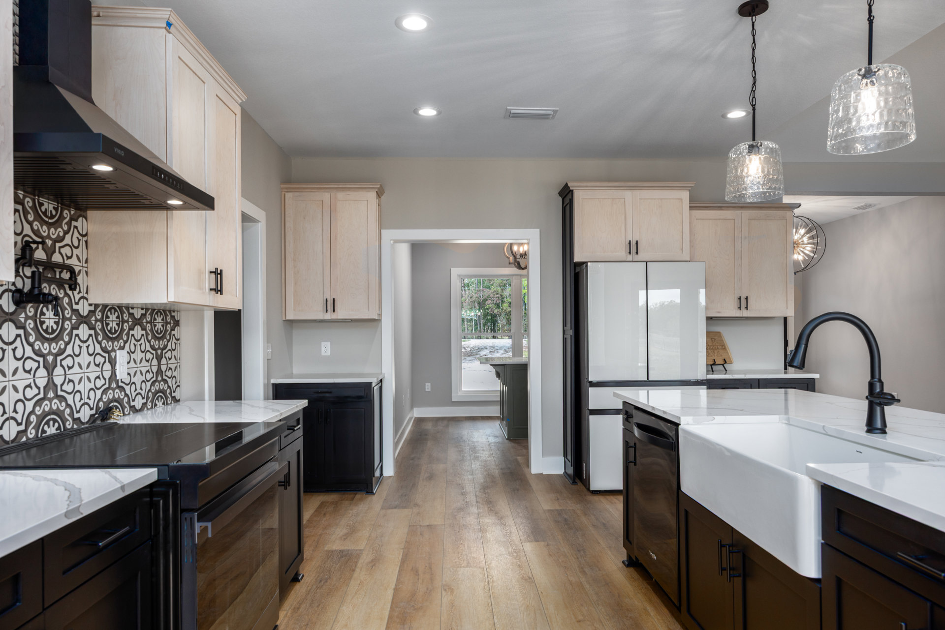 Kitchen with natural wood flooring, white cabinetry, stainless steel sink, black metal chandelier with glass shades, stone countertops, and modern plumbing fixtures.