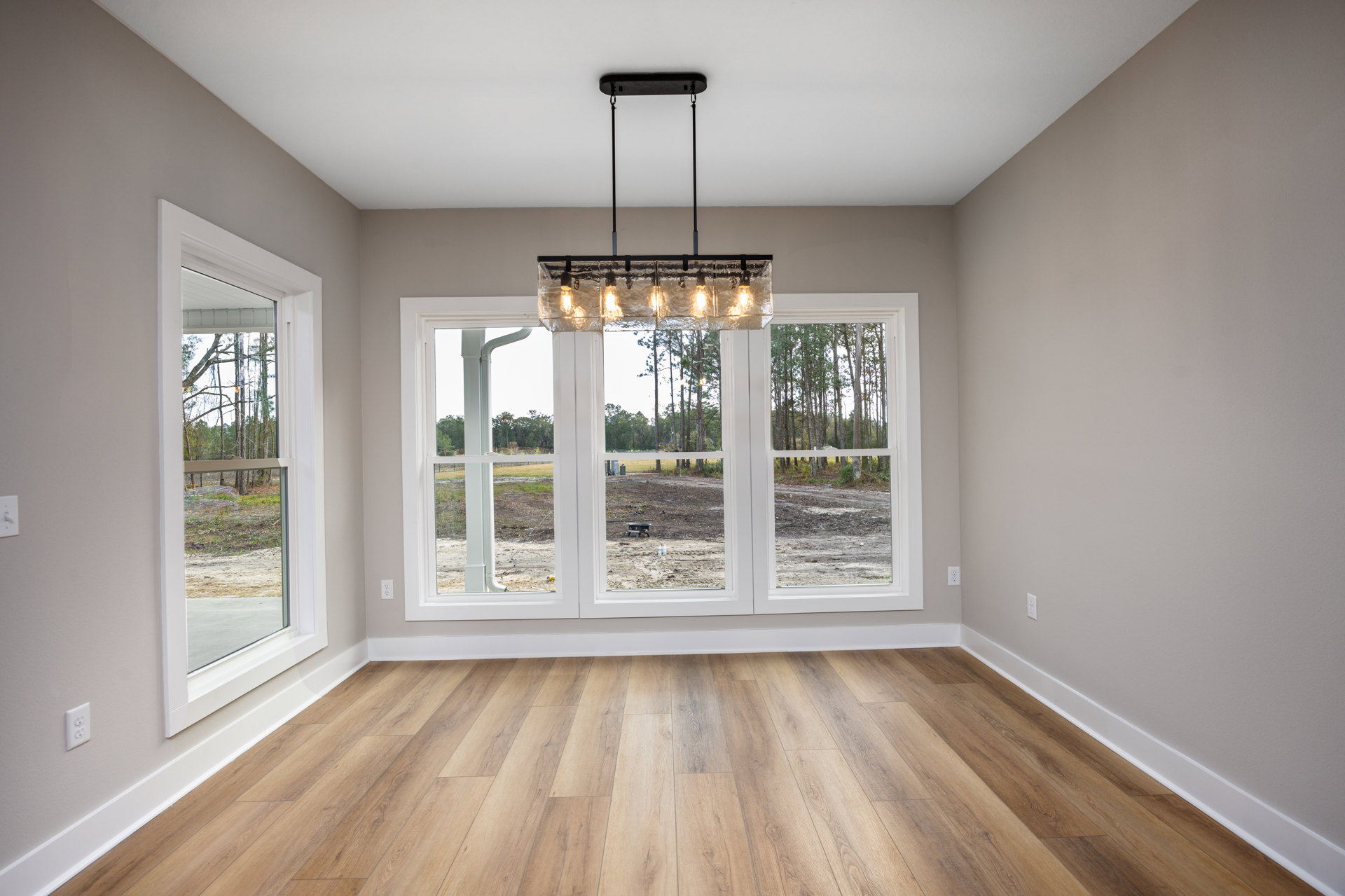 Wood flooring in a bright room with large windows, white walls, glass block light fixture, and view of trees outside