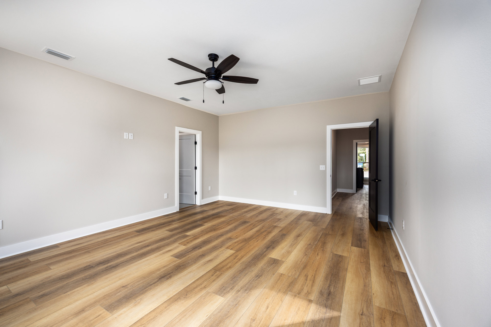 Ceiling fan with light fixture mounted on white plaster ceiling, hardwood flooring, white door with black handle open to adjacent room, neutral wall finishes