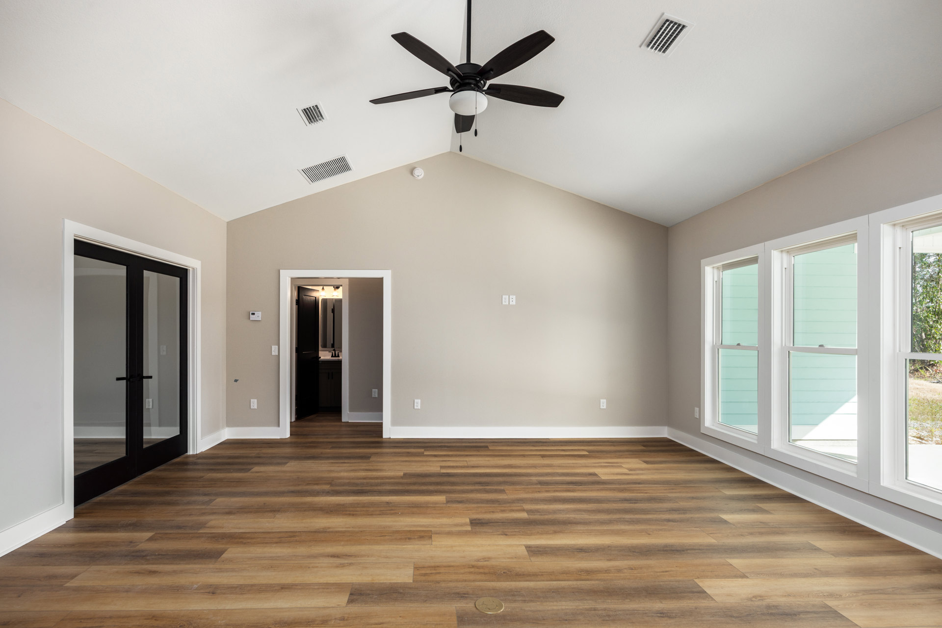 Ceiling fan with light fixture, wood laminate flooring, glass door with black handle, bathroom visible with mirror and black door, ceiling vent, coin on floor