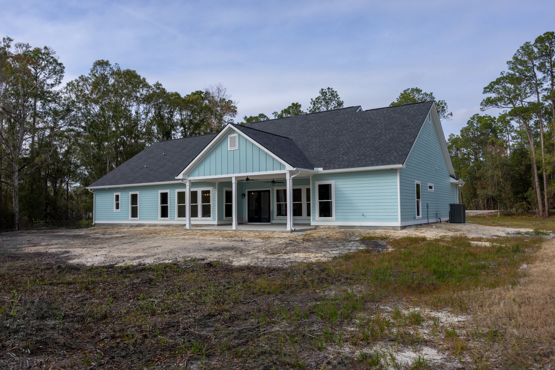 Blue siding house with spacious front porch, white columns, white-framed windows, single door with porch light, dirt patch yard, large black heater on concrete walkway, cloudy sky