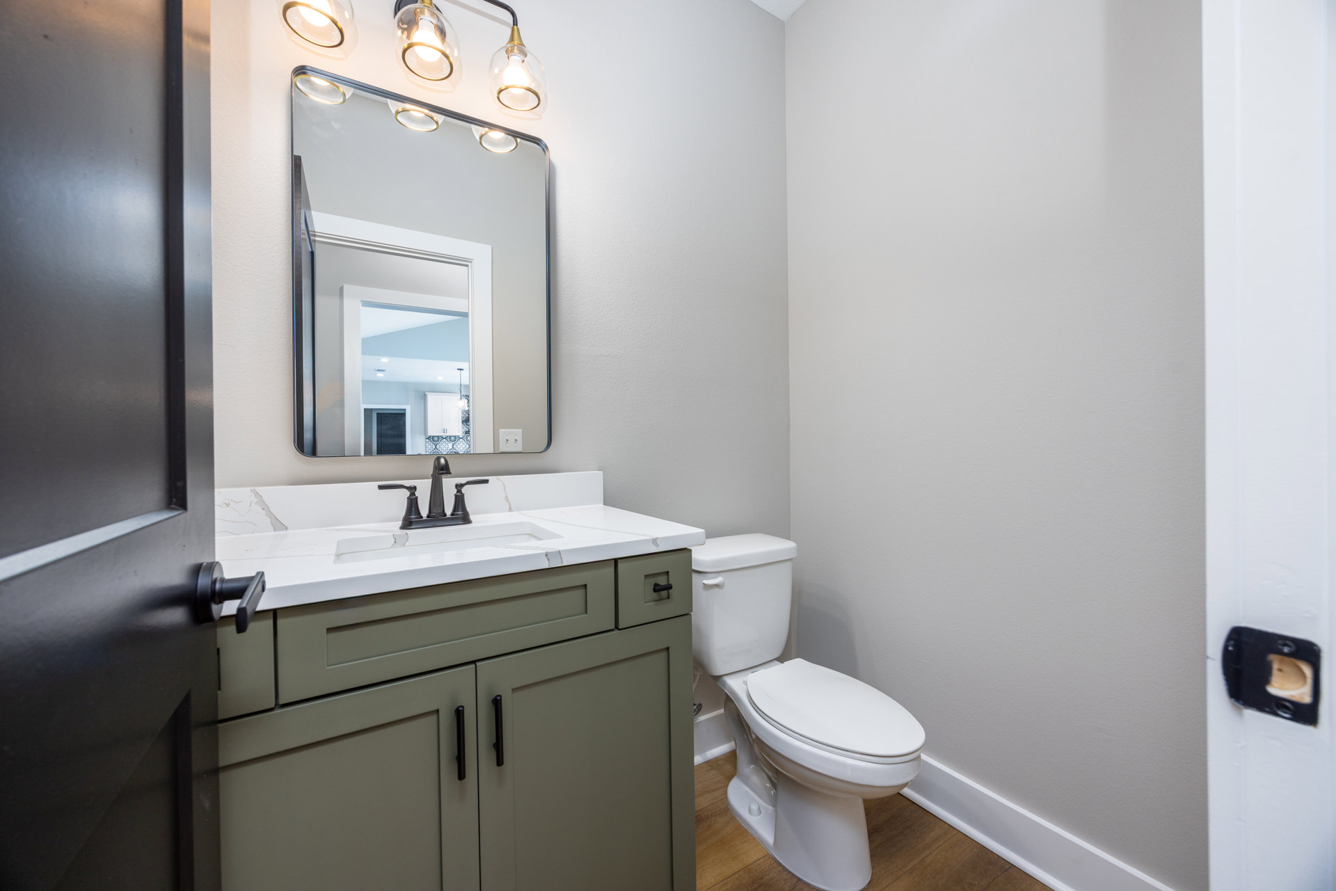 Modern bathroom featuring a rectangular mirror with integrated lighting above a white countertop and sink, chrome faucet, white toilet with lid closed, light gray tile walls, and a