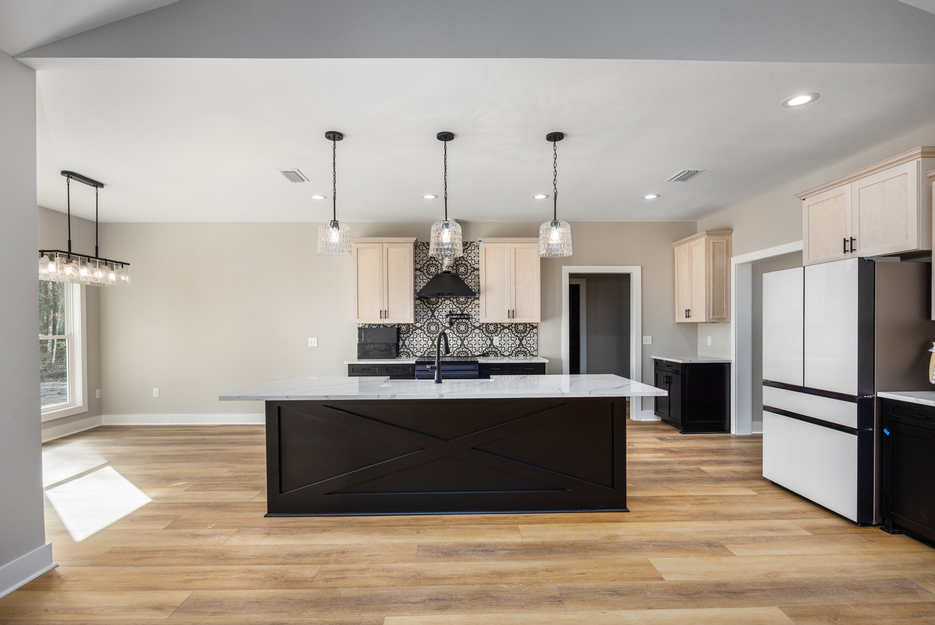 Spacious kitchen featuring a large central island with white countertop, black cabinetry, stainless steel refrigerator, and modern pendant light fixtures