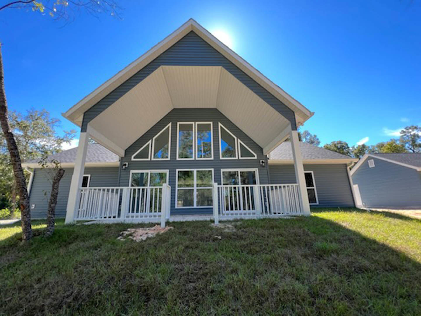 Two-story house with blue siding, white porch railing, grassy front yard, mature tree, and attached blue garage with white roof.