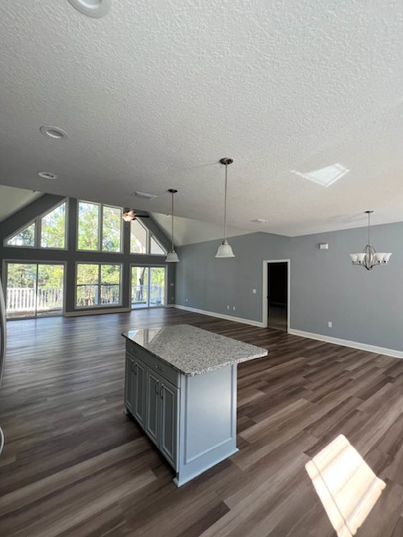 Open-concept kitchen with white marble-topped island, hardwood floors, multiple windows, and pendant light fixtures.