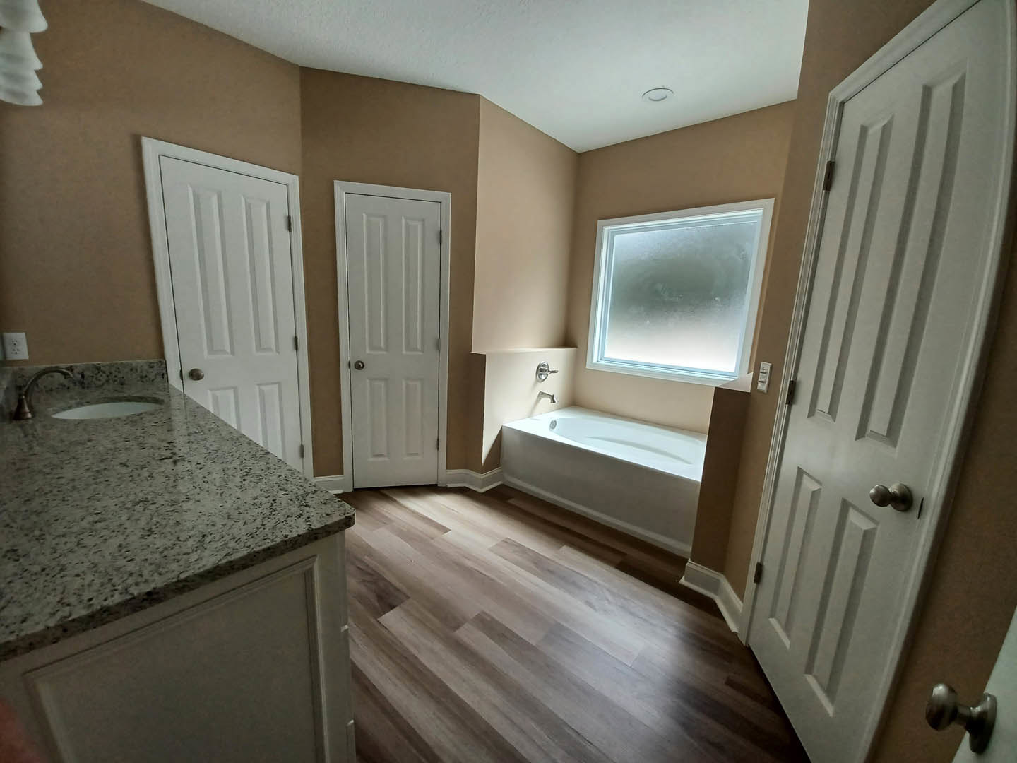 Bathroom with freestanding tub, rectangular sink on wood vanity, frosted window, white door with silver handle, wood plank flooring