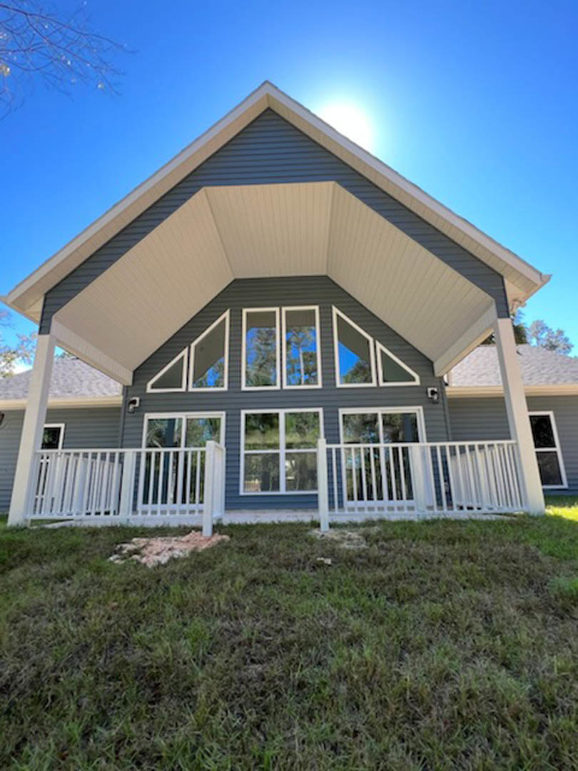Front porch with white railing, light-colored siding, large window reflecting trees, manicured grass lawn