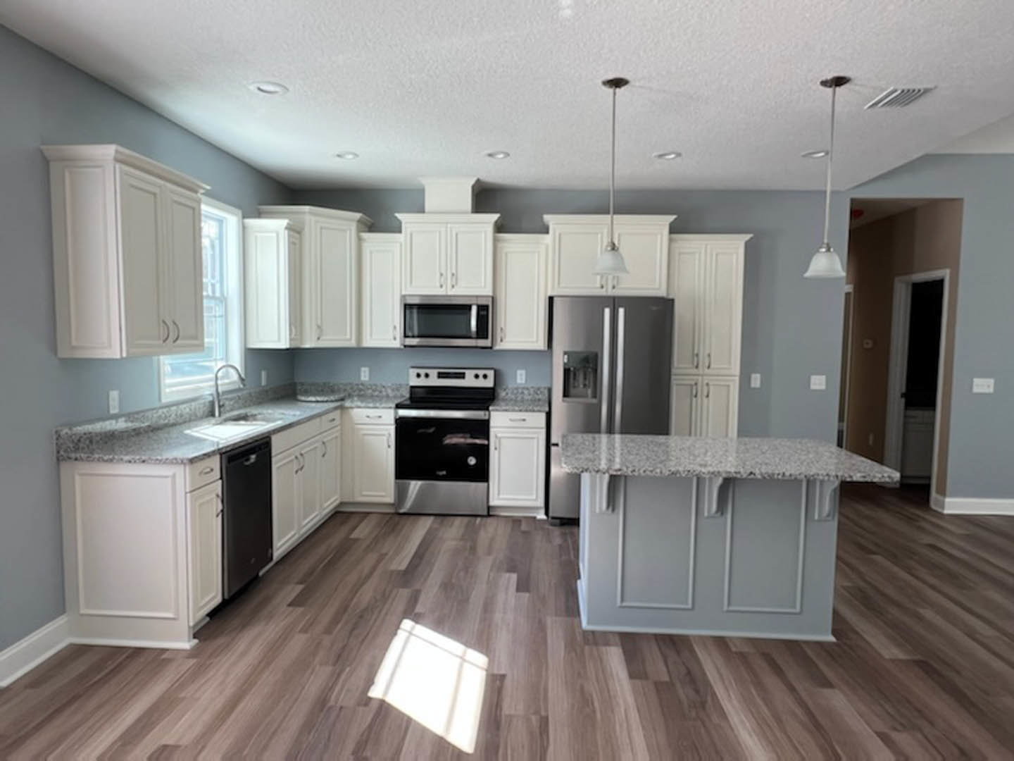 White kitchen cabinets, granite countertops, stainless steel appliances, wood flooring, white towel on floor