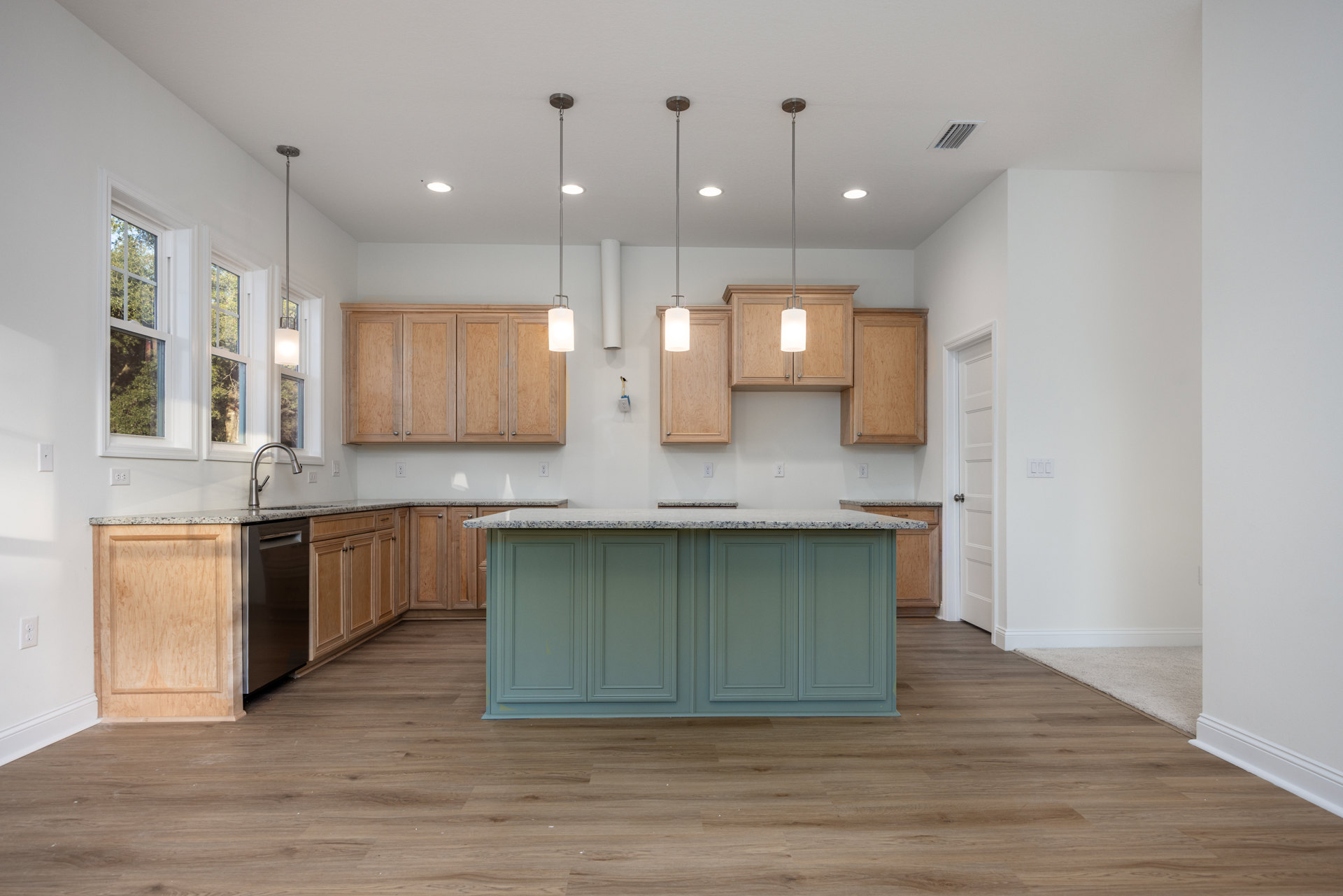 Kitchen with central marble-topped island, wood cabinets featuring silver handles, tile flooring, large window overlooking trees, and carved wood panel detailing