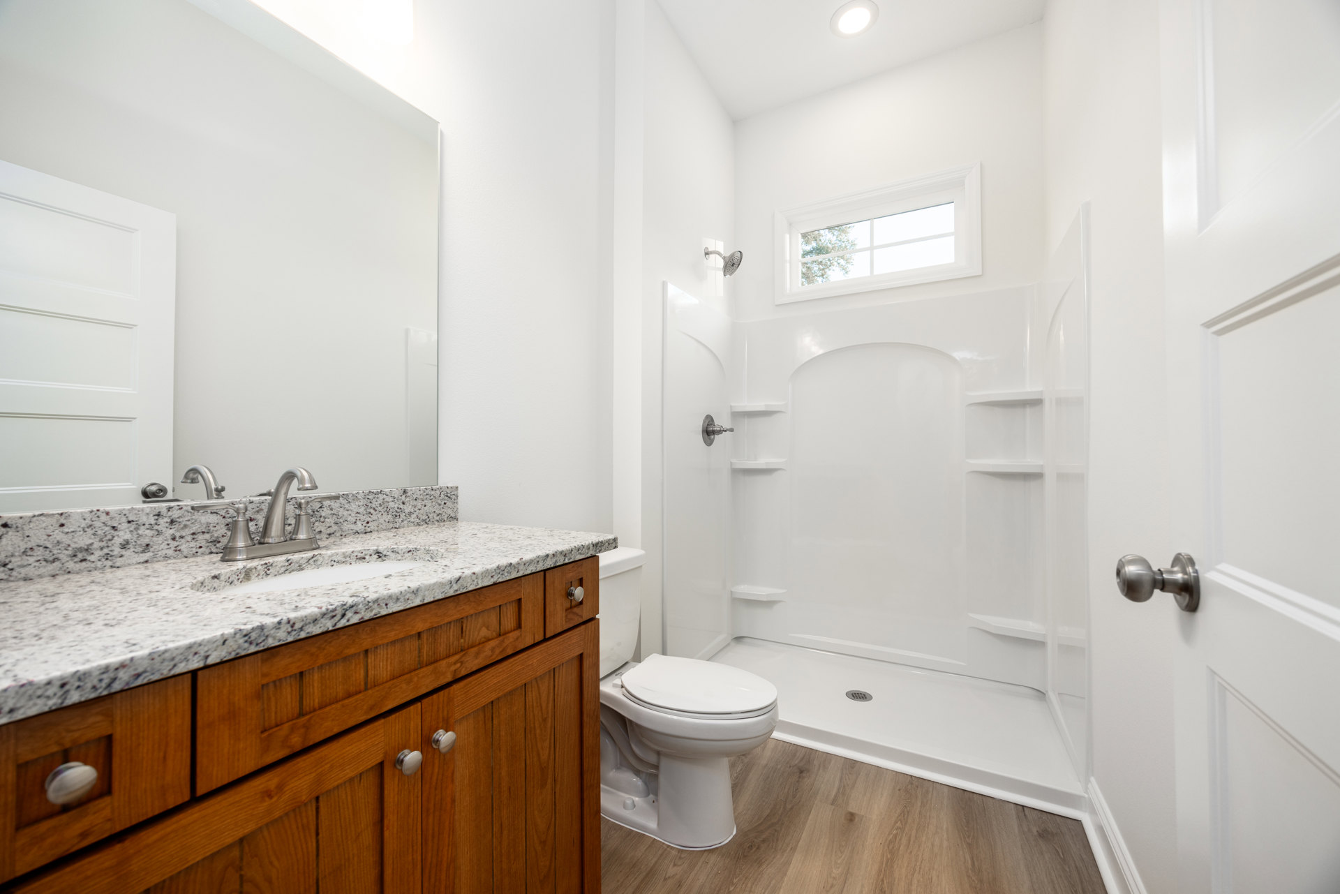Bathroom with white tile floor, white toilet, built-in sink with light wood cabinetry, chrome faucet, and frosted window above shower enclosure