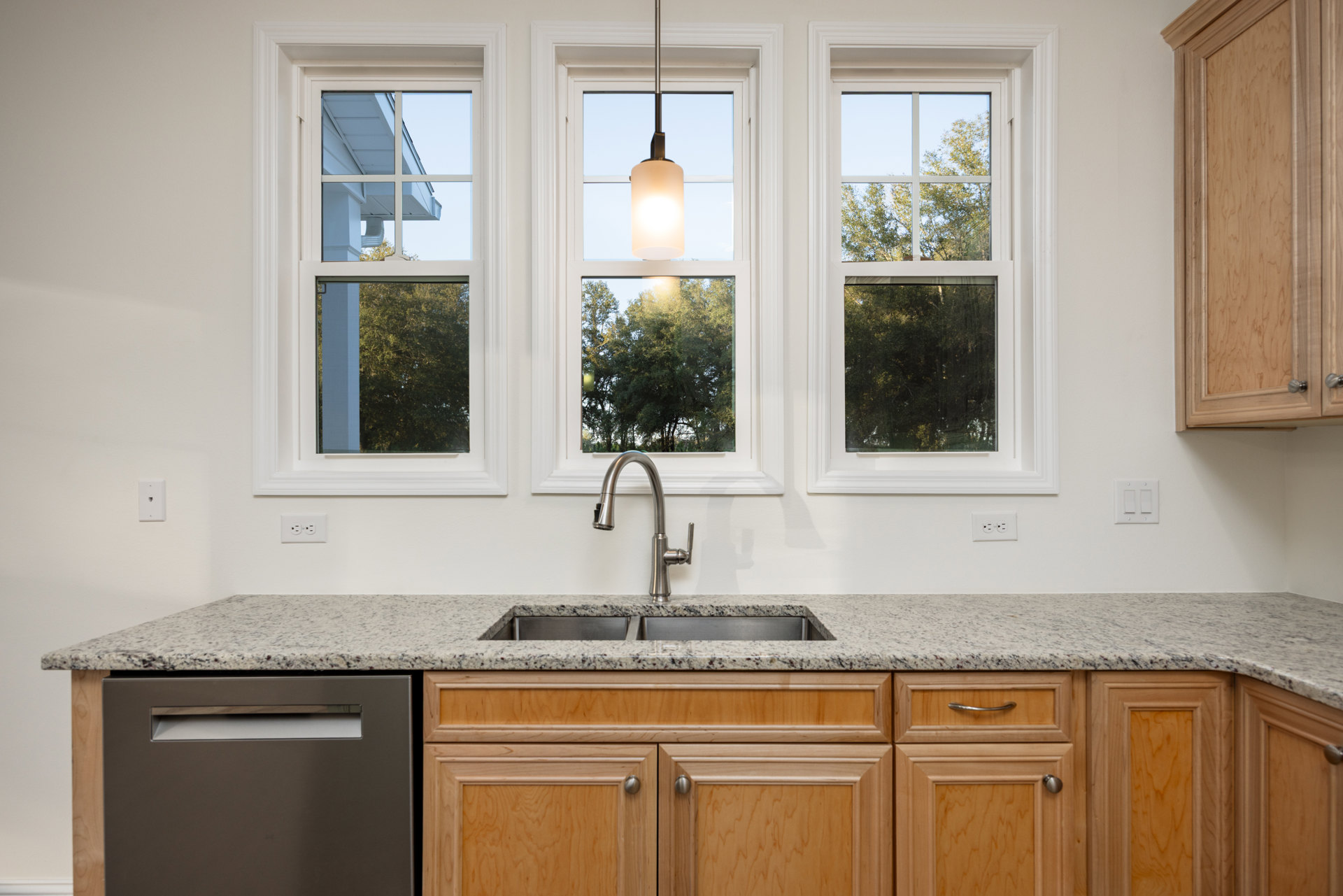 Bright kitchen with white cabinetry, stainless steel sink under large windows, stone countertop, modern faucet, and natural light illuminating wood floors