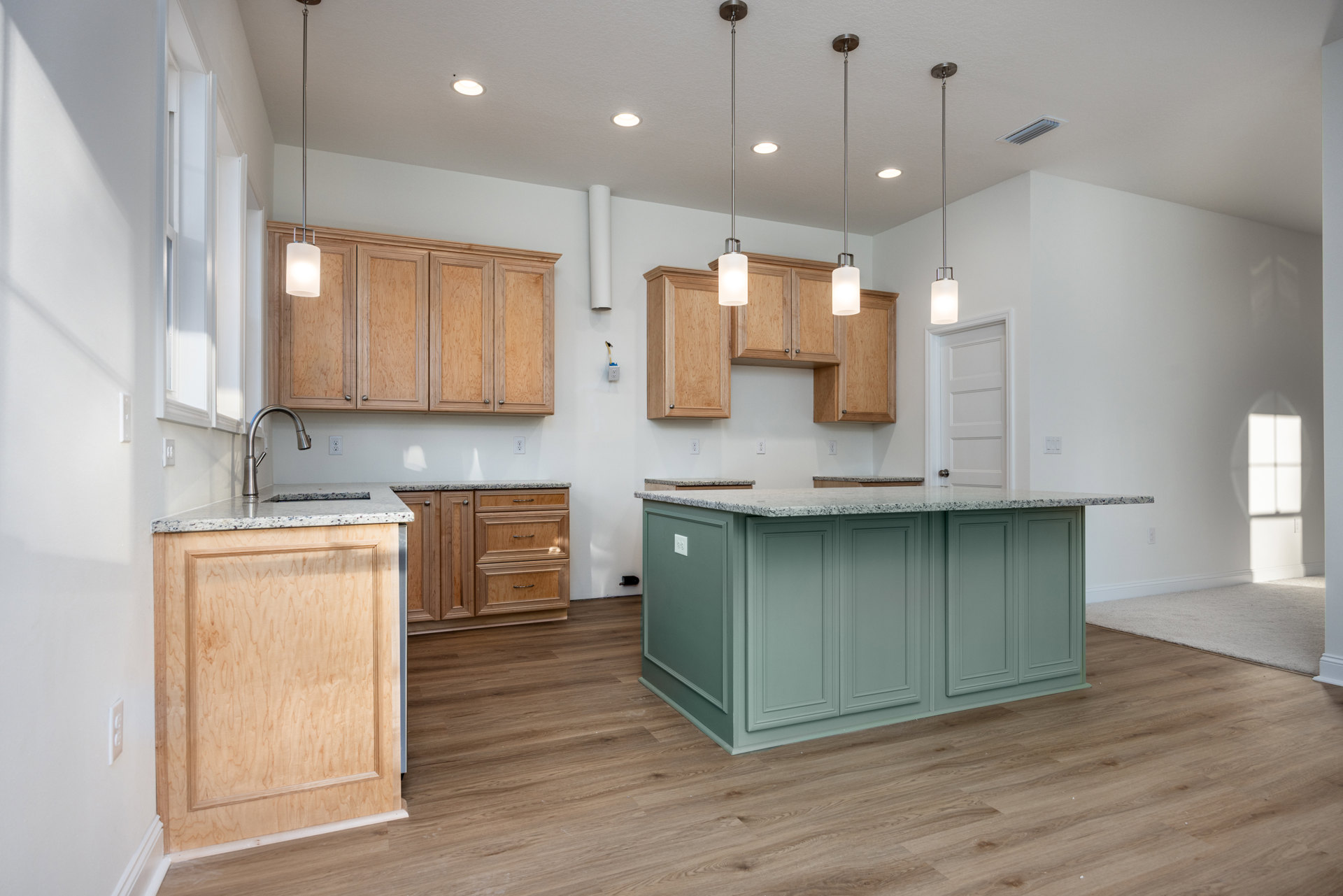 Marble-topped kitchen island with built-in sink and chrome faucet, white cabinetry, wood paneled door, hardwood flooring, pendant light fixture, and close-up of drawer front