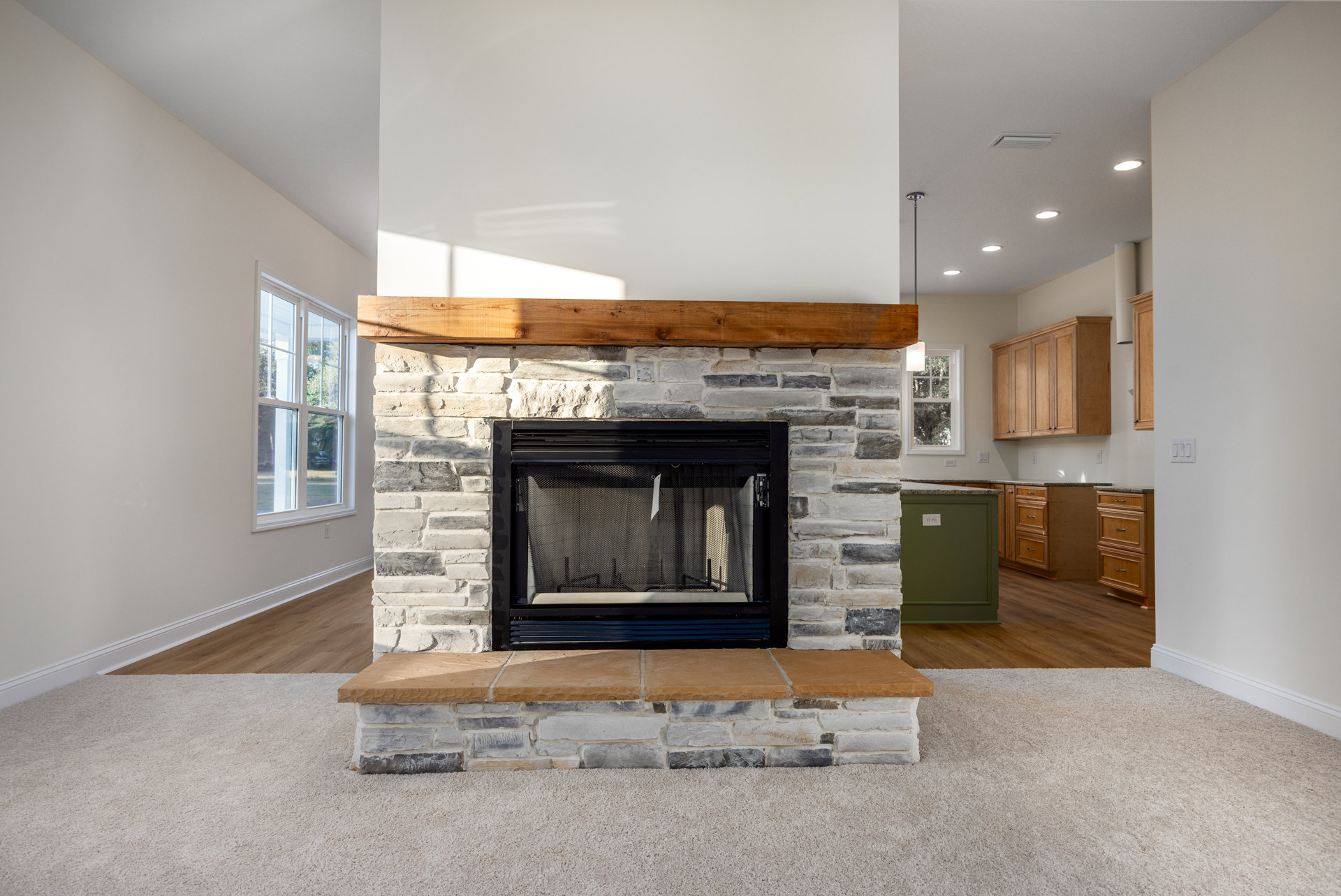 Stone fireplace with black metal screen and wood mantel, surrounded by multi-pane windows, green accent wall, and white electrical outlet.