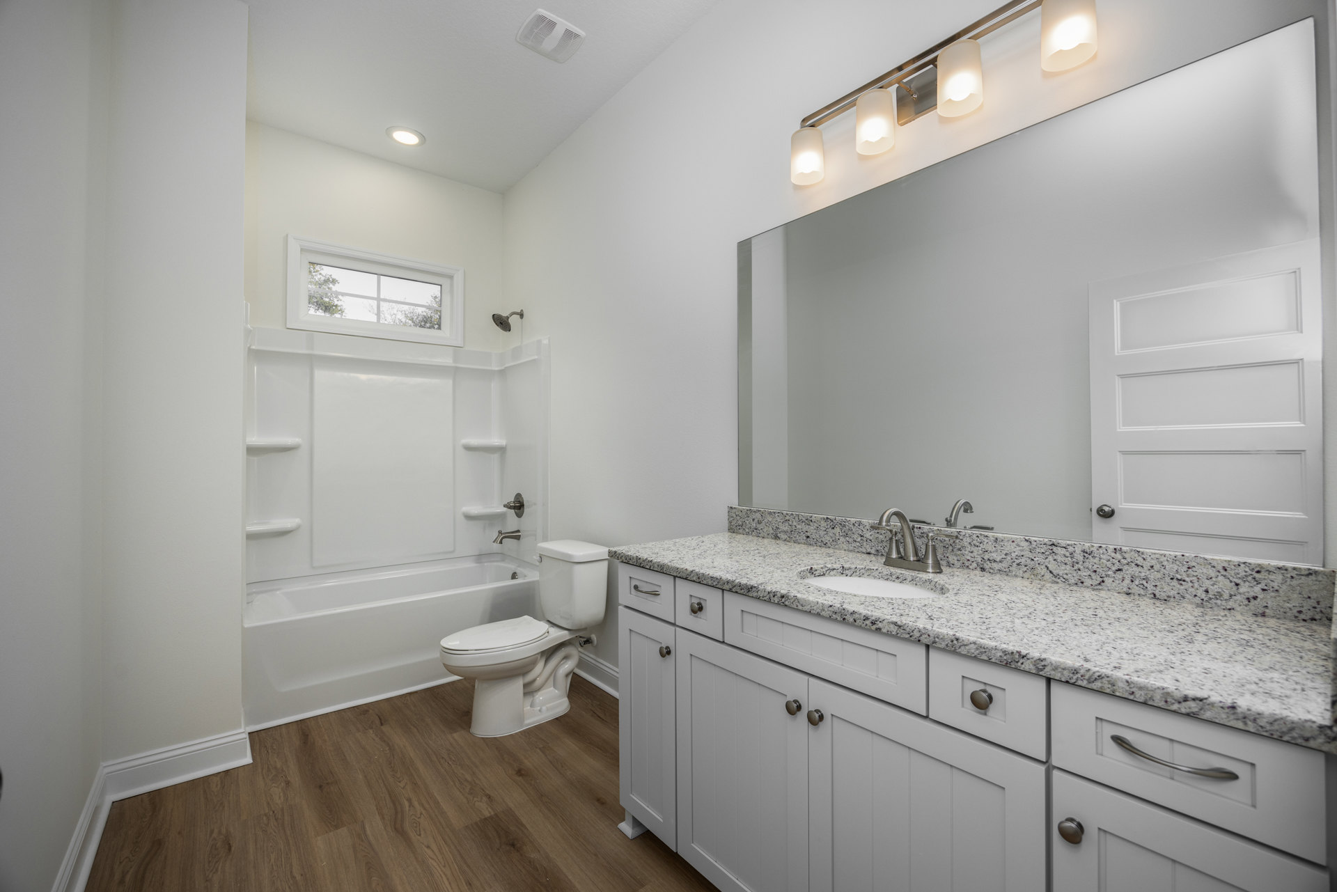 Modern bathroom with white toilet, rectangular sink on stone countertop, glass-enclosed shower, light fixture with white shade, large window overlooking trees, gray tile floor, and