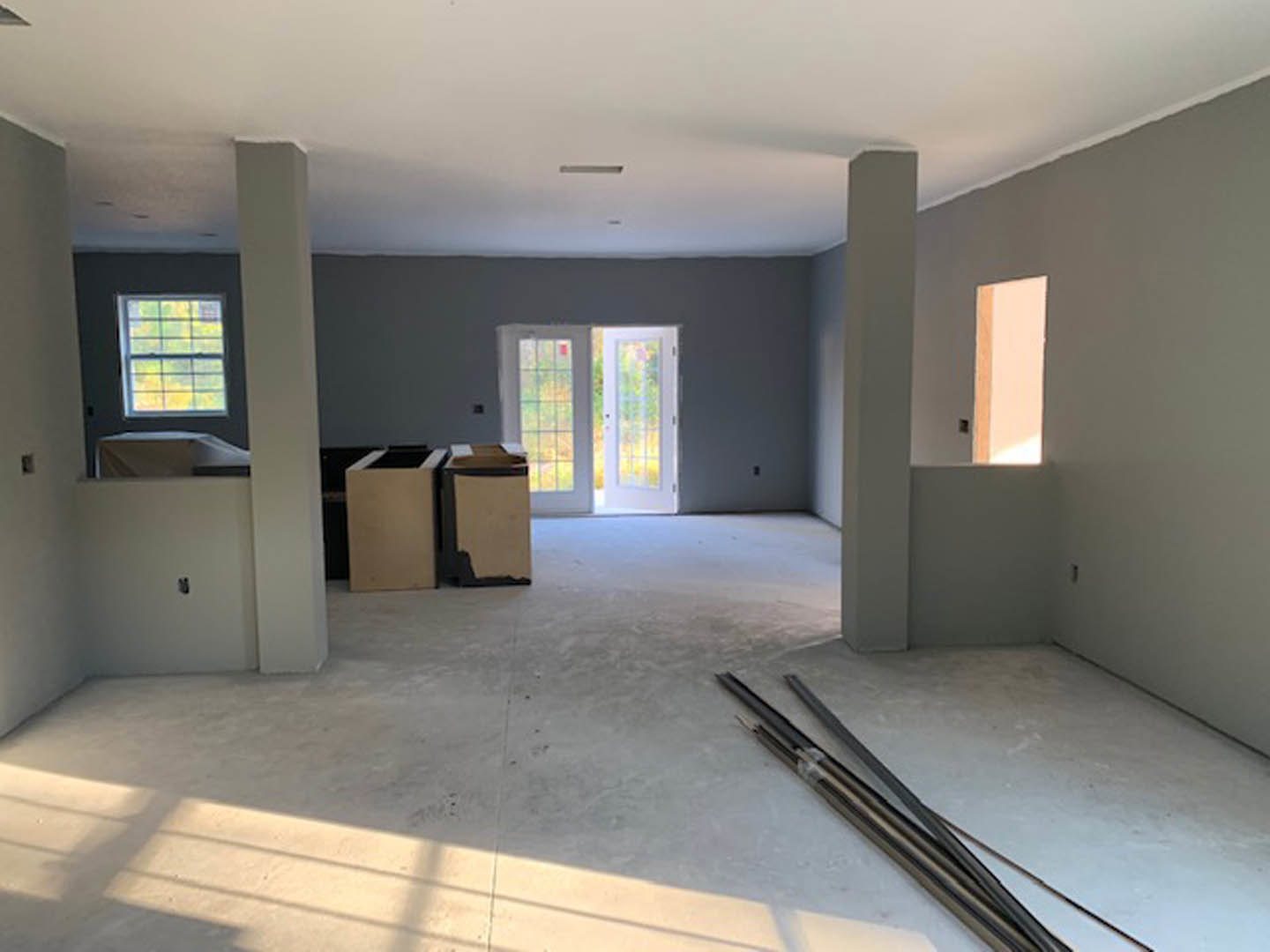 White-walled room featuring double glass-paneled doors, multiple windows with white trim, light wood flooring, and a metal curtain rod.