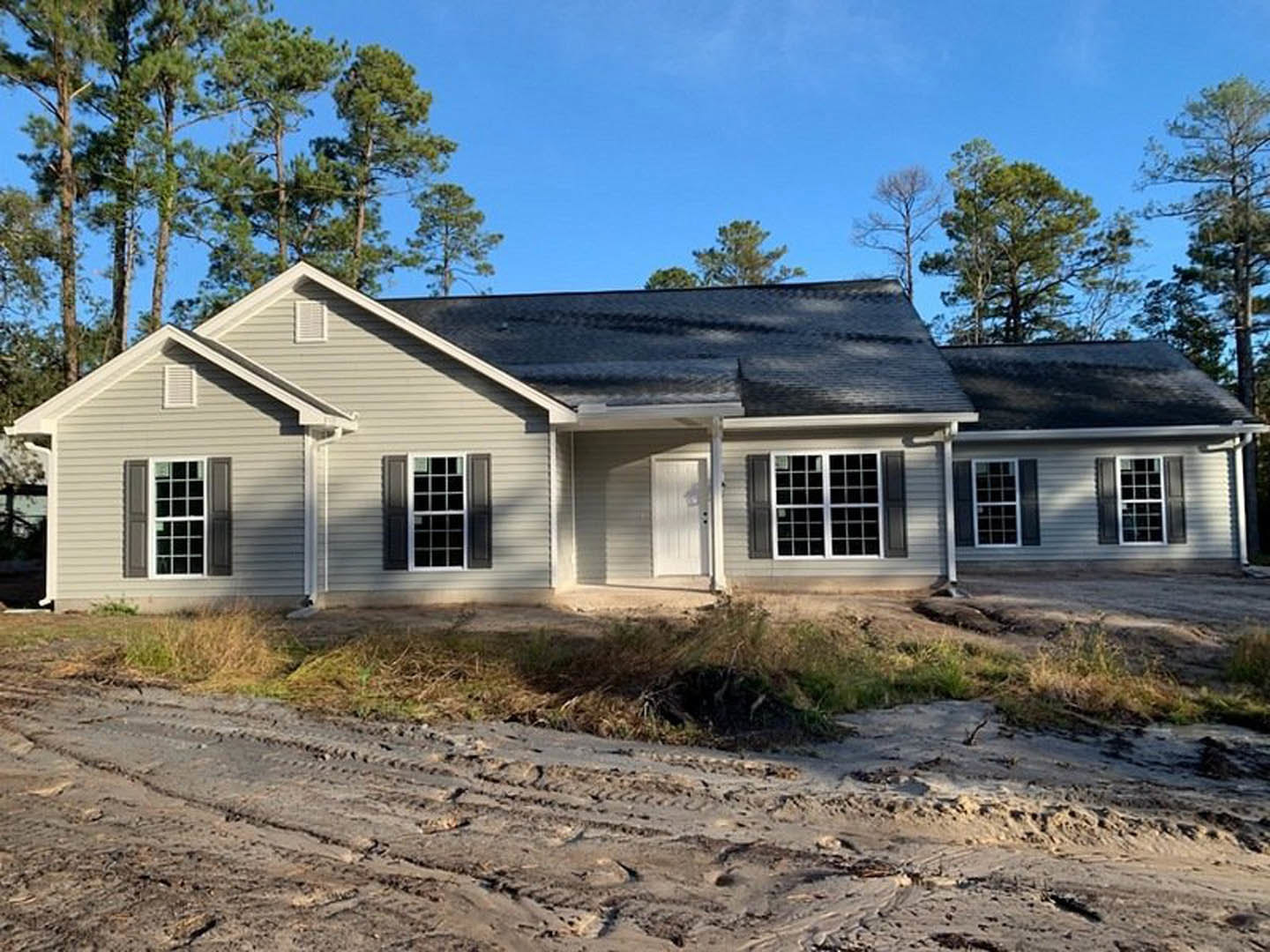 White door and multiple square windows on a house with a black roof, tire tracks visible on sandy dirt road under clear blue sky.