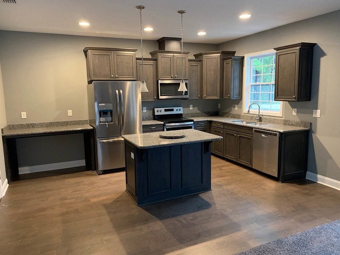 Modern kitchen featuring stainless steel refrigerator with water dispenser, built-in microwave, granite-topped island, stove, white cabinetry, and undermount sink
