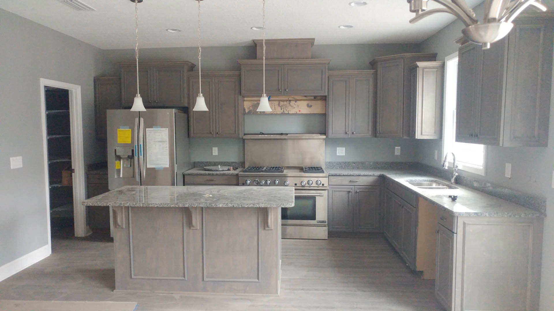 Grey shaker cabinets, speckled granite countertops, stainless steel appliances, white subway tile backsplash, refrigerator with papers attached, undermount sink, and a white wall