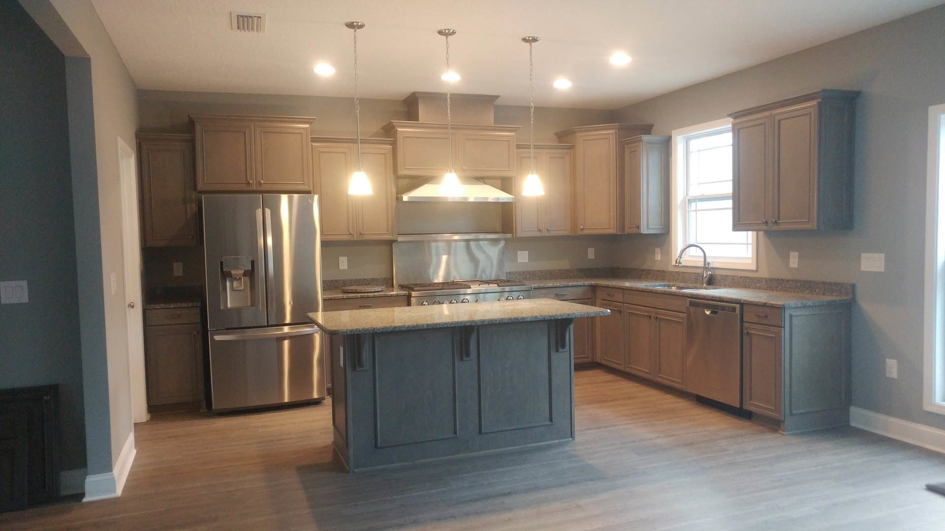 Open kitchen with central island, stainless steel refrigerator with ice and water dispenser, white cabinetry with black hardware, built-in stove and oven, light fixture on blue