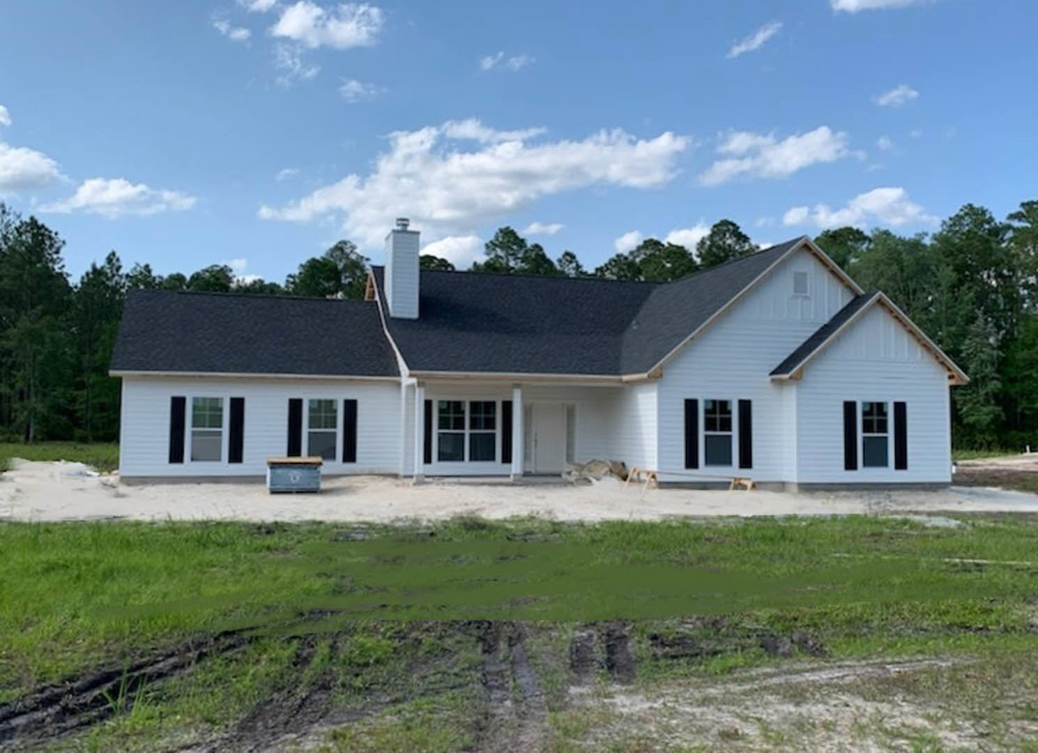 White siding house with black shingle roof, large windows, green lawn, blue sky with scattered clouds