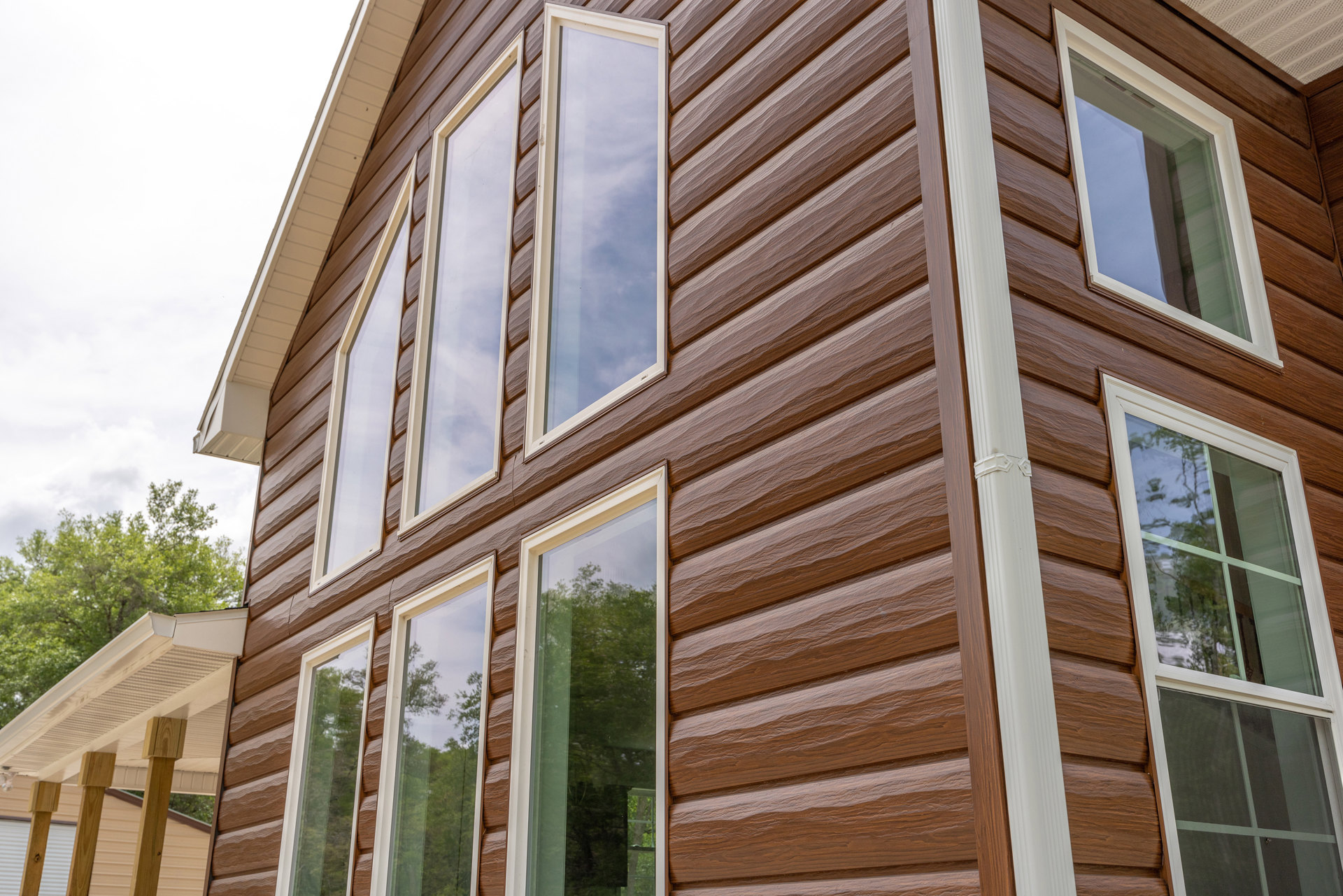 Two-story custom home with white siding, numerous large windows, and surrounding mature trees under a clear blue sky