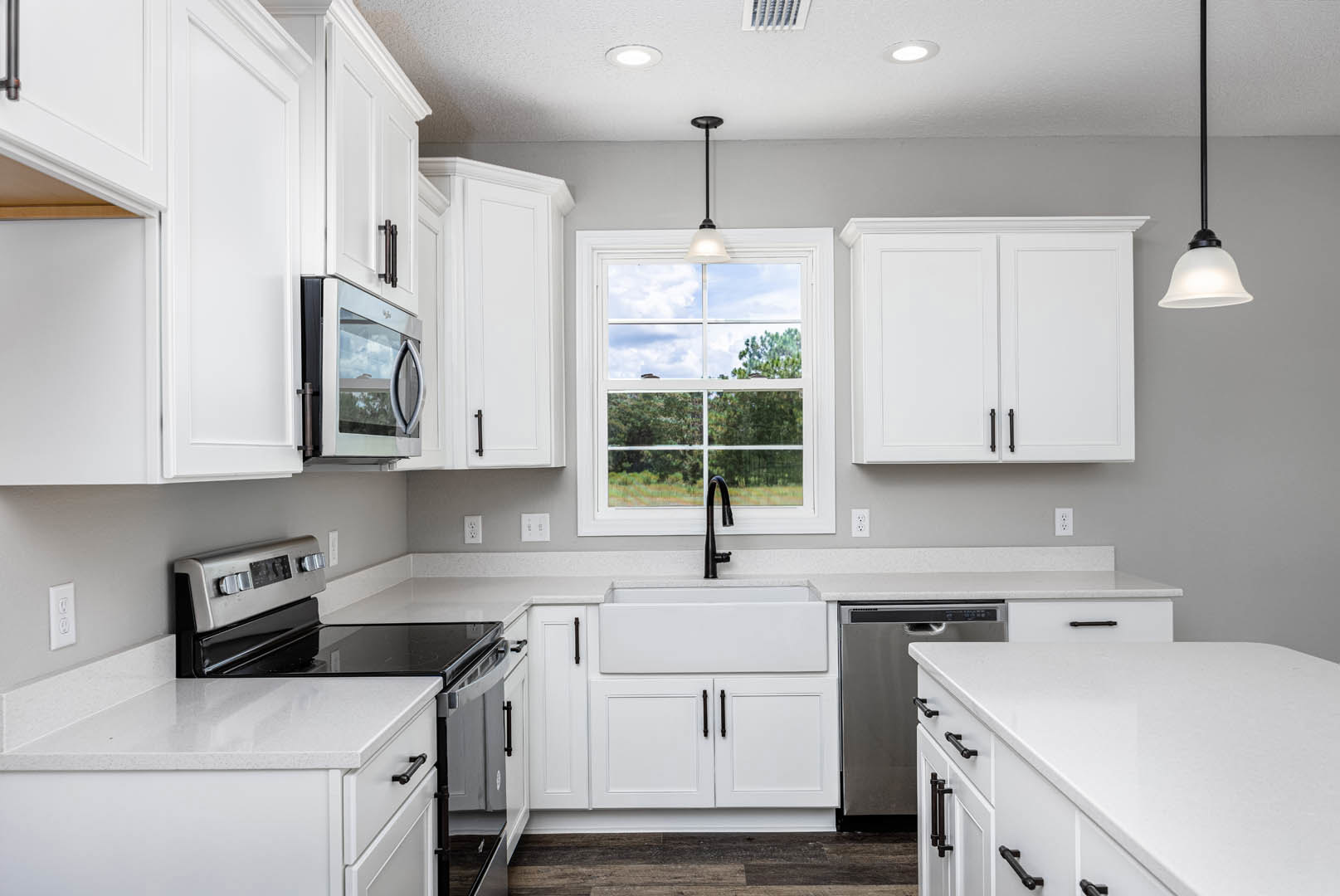 White kitchen cabinets, black stove and microwave, white countertop, stainless sink beneath window with outdoor view, black appliance accents