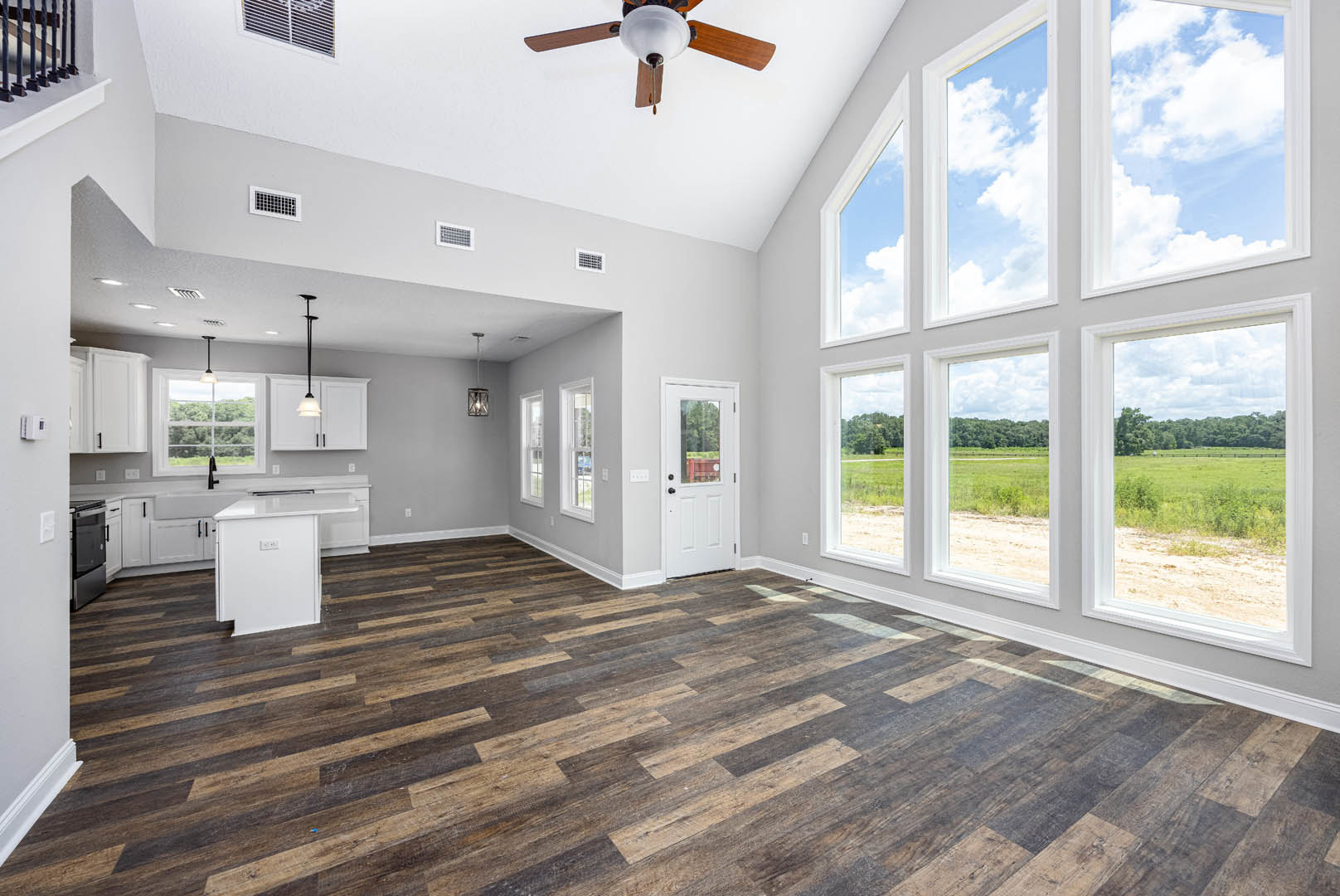 Open room with wood flooring, ceiling fan with light, black and white oven, white door with window, white table, and visible light switch on wall