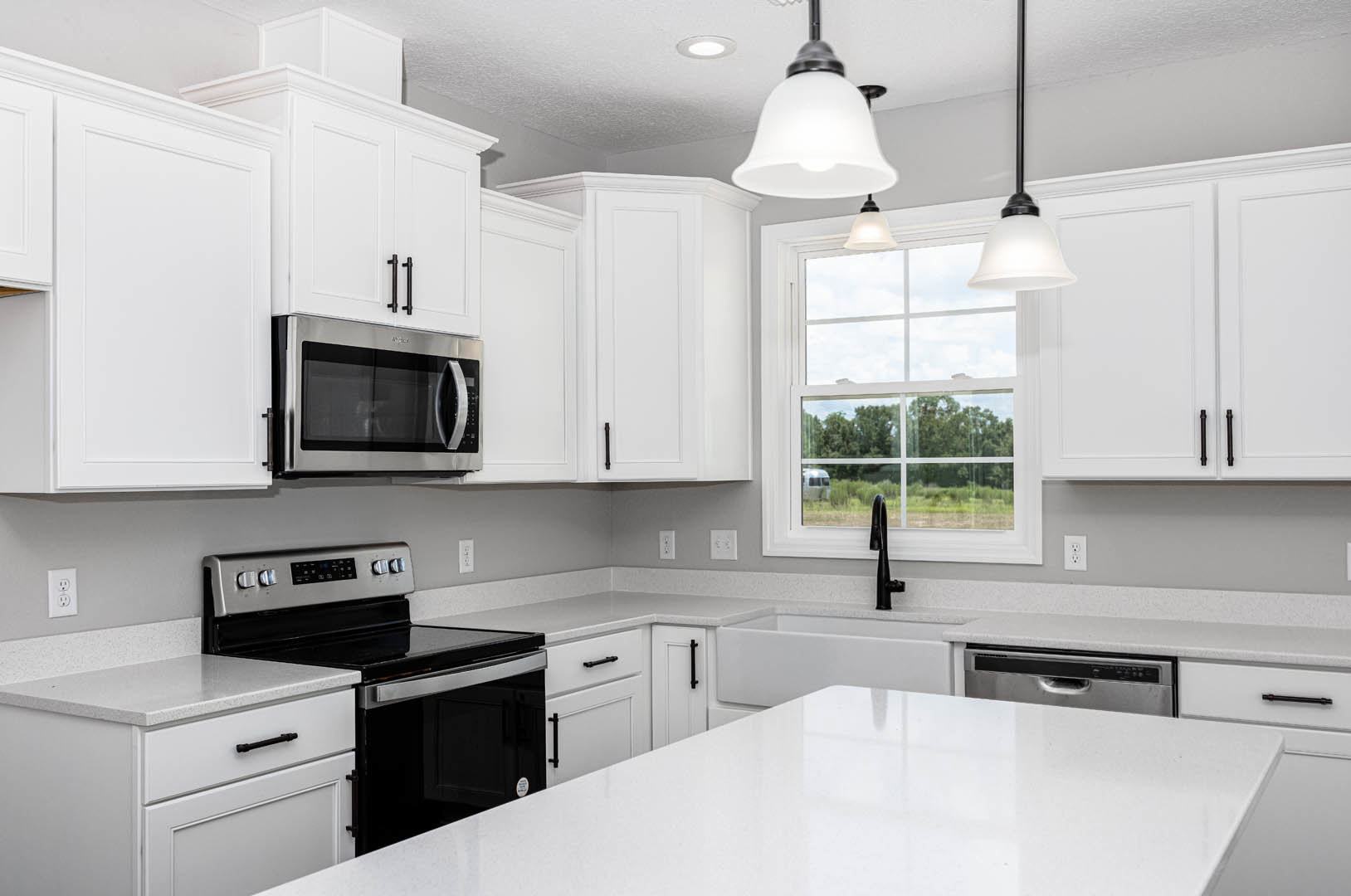 White kitchen with shaker cabinets, quartz countertop, stainless steel stove and microwave, pendant light fixture, and black cabinet handles.
