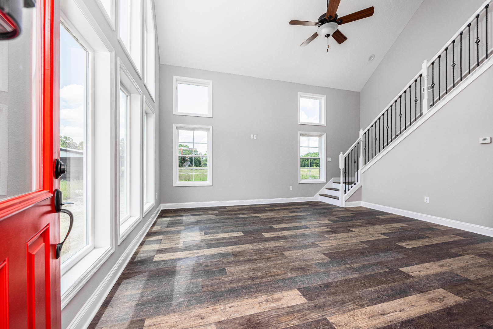 Wood flooring, white staircase, ceiling fan with light, square window with white frame overlooking green lawn, neutral walls