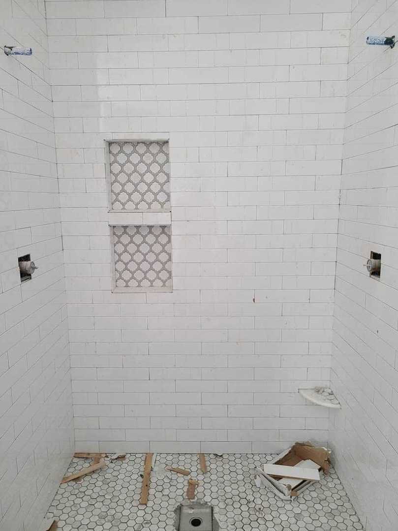 White tiled shower with built-in shelf, window above, grey tile border, cardboard box and exposed hole in bathroom floor