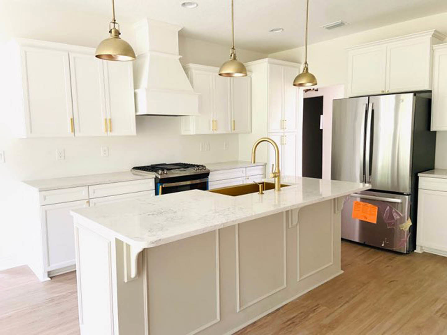 White shaker cabinets, stainless steel refrigerator with a sticker on the door, stone countertops, undermount sink, modern stove, light tile flooring