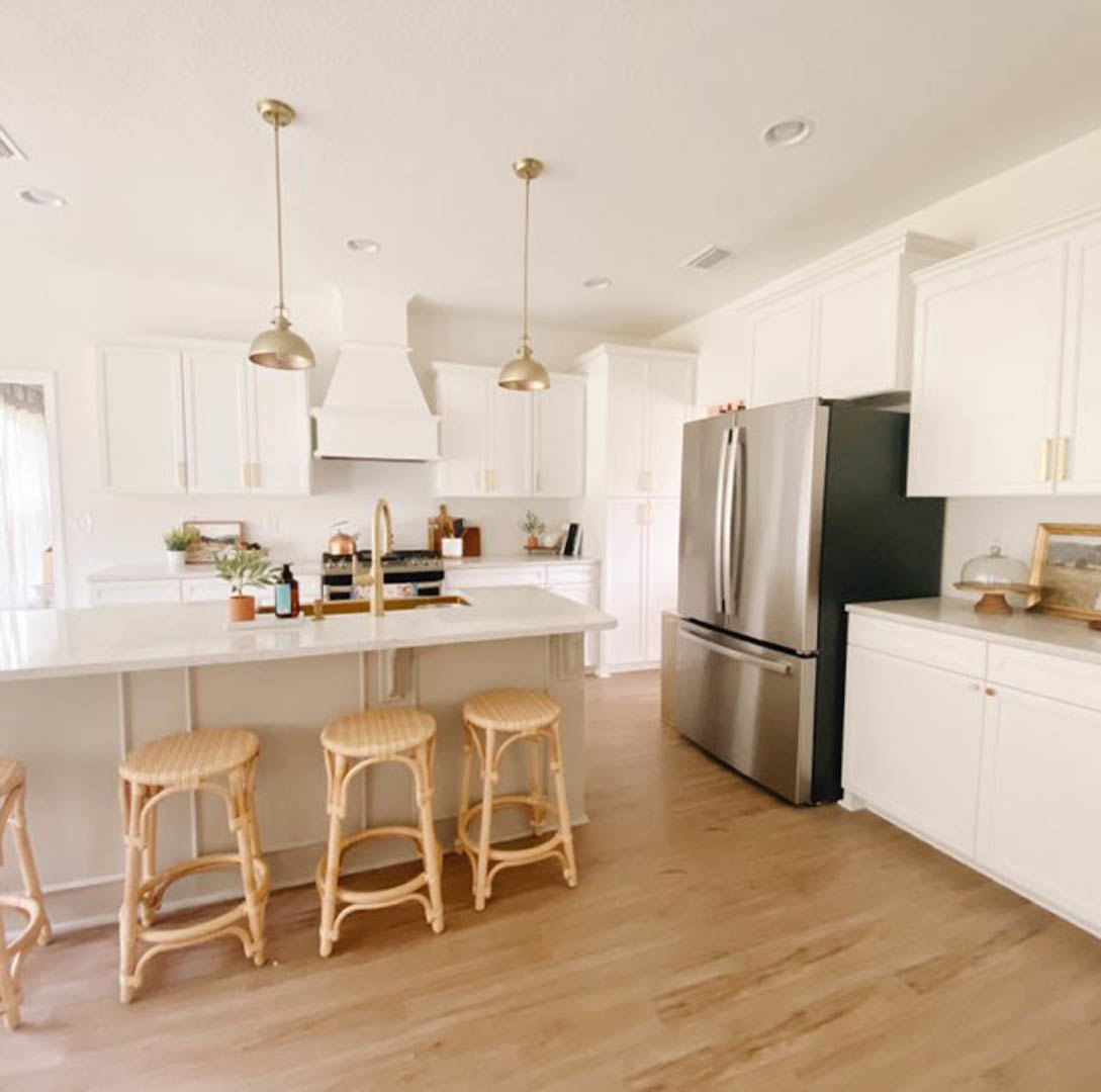 White shaker cabinets, stainless refrigerator, quartz countertops, island bar with wooden stools, light hardwood floors, glass dome tray on counter