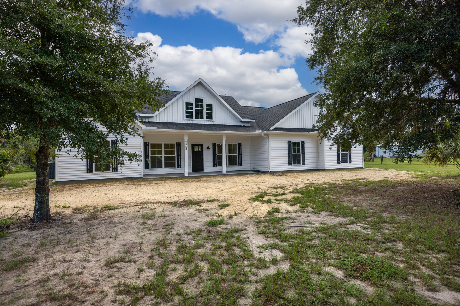 White siding house with black front door, white-framed windows, dirt pathway, and large tree in front yard