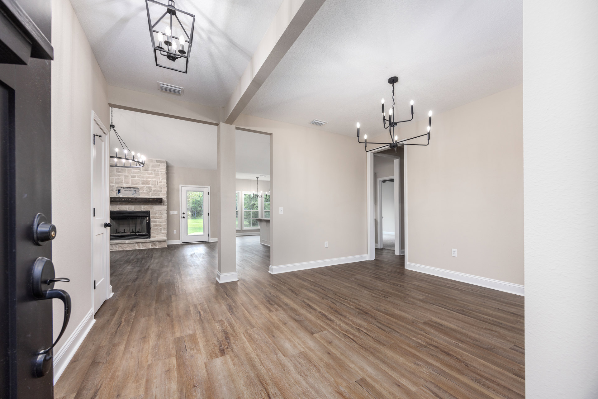 Hardwood floored living space featuring a black chandelier, white pillars, glass fireplace, and a door opening to grassy yard and trees
