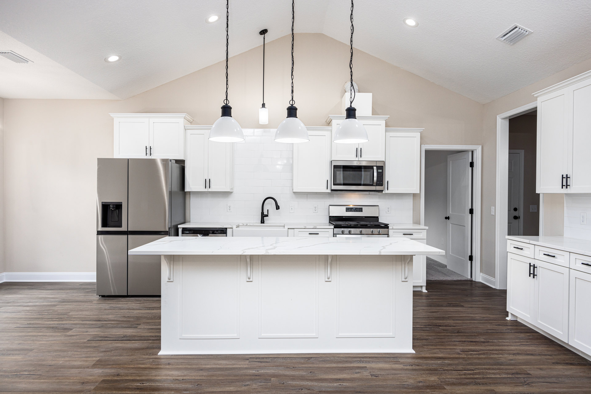 Spacious kitchen featuring a large white island with quartz countertop, stainless steel refrigerator with black handle, white cabinetry, built-in microwave, black faucet set