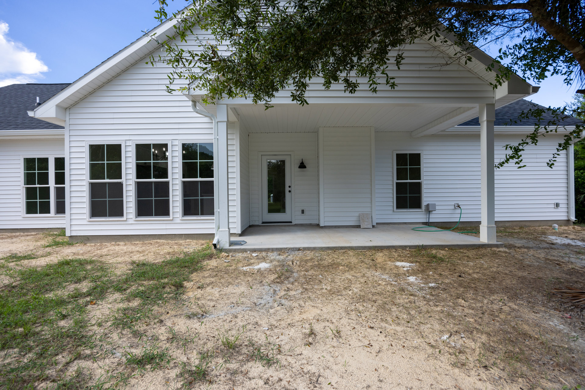 White siding house with covered front porch, white door with glass panel, multi-pane windows, tree beside entry, dirt patch in front yard