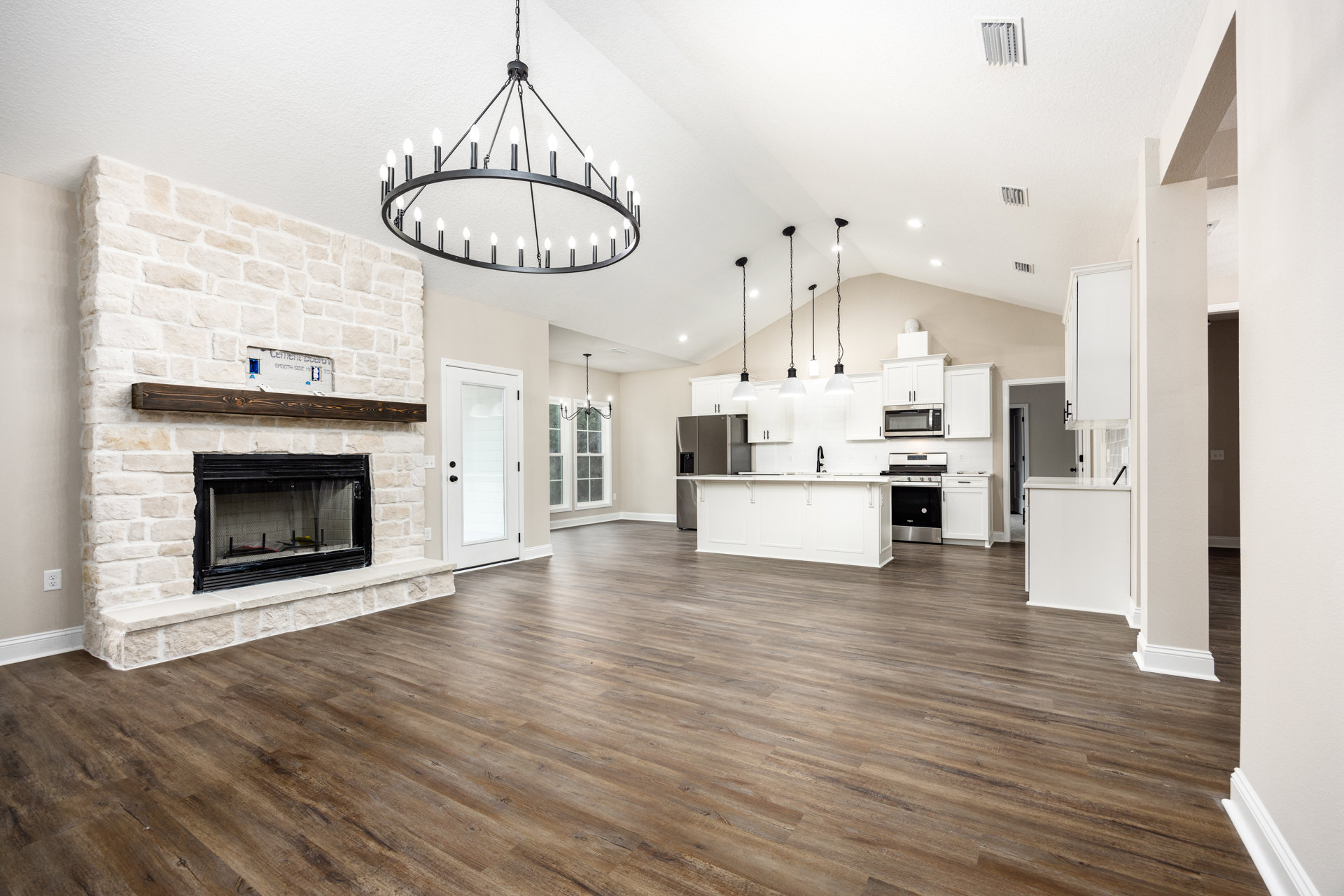 Spacious open floor plan featuring hardwood floors, a central fireplace with a screen, large white kitchen cabinetry, white stove with black door, chandelier lighting, and a white