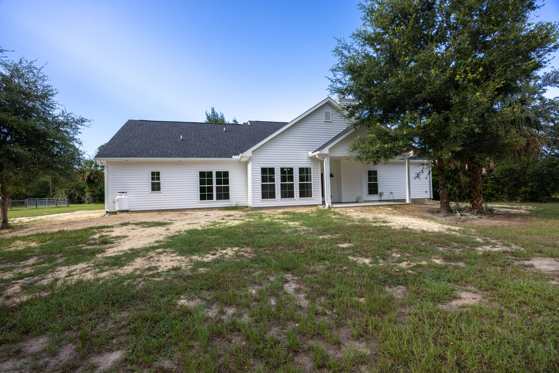 White siding house with multiple pane windows, dark roof, green lawn, and mature trees in front yard
