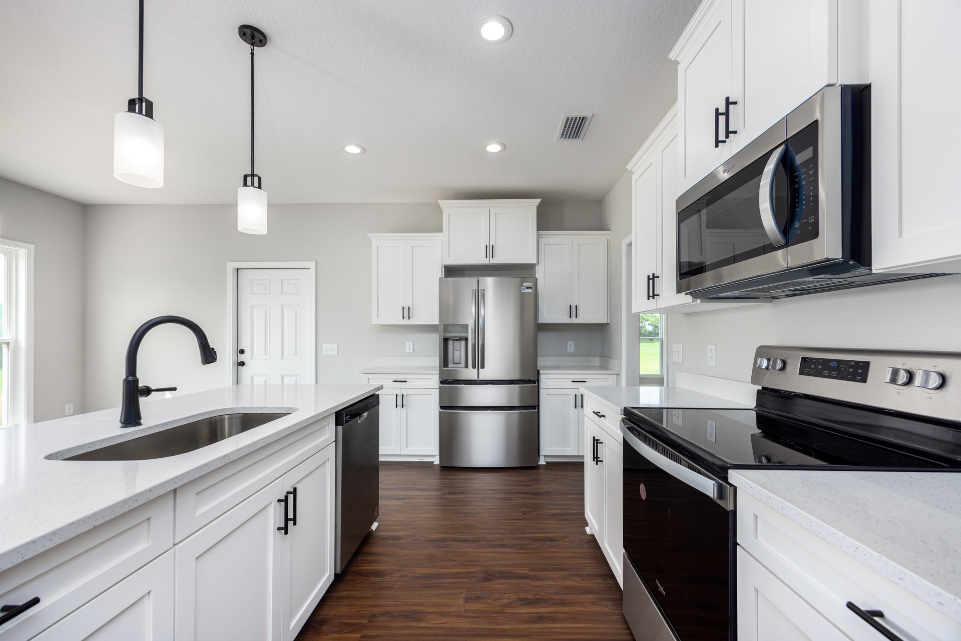 White shaker cabinets, stainless steel refrigerator with water dispenser, built-in microwave, quartz countertops, undermount sink, modern ceiling light fixture, and ceiling vent.