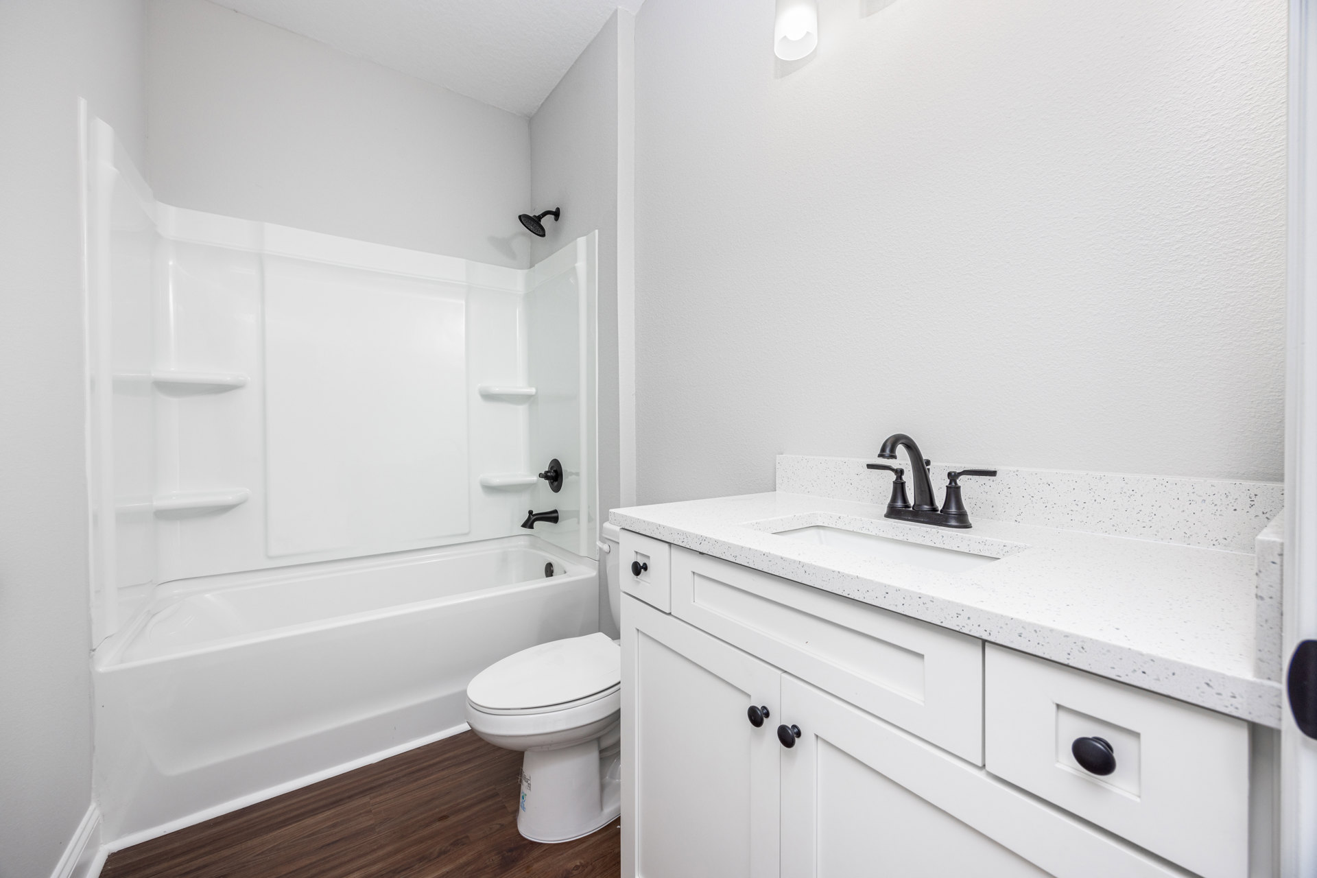 White bathroom featuring a rectangular sink with chrome faucet, freestanding bathtub, closed-lid toilet, black cabinet knob, and white light fixture mounted on tiled wall.