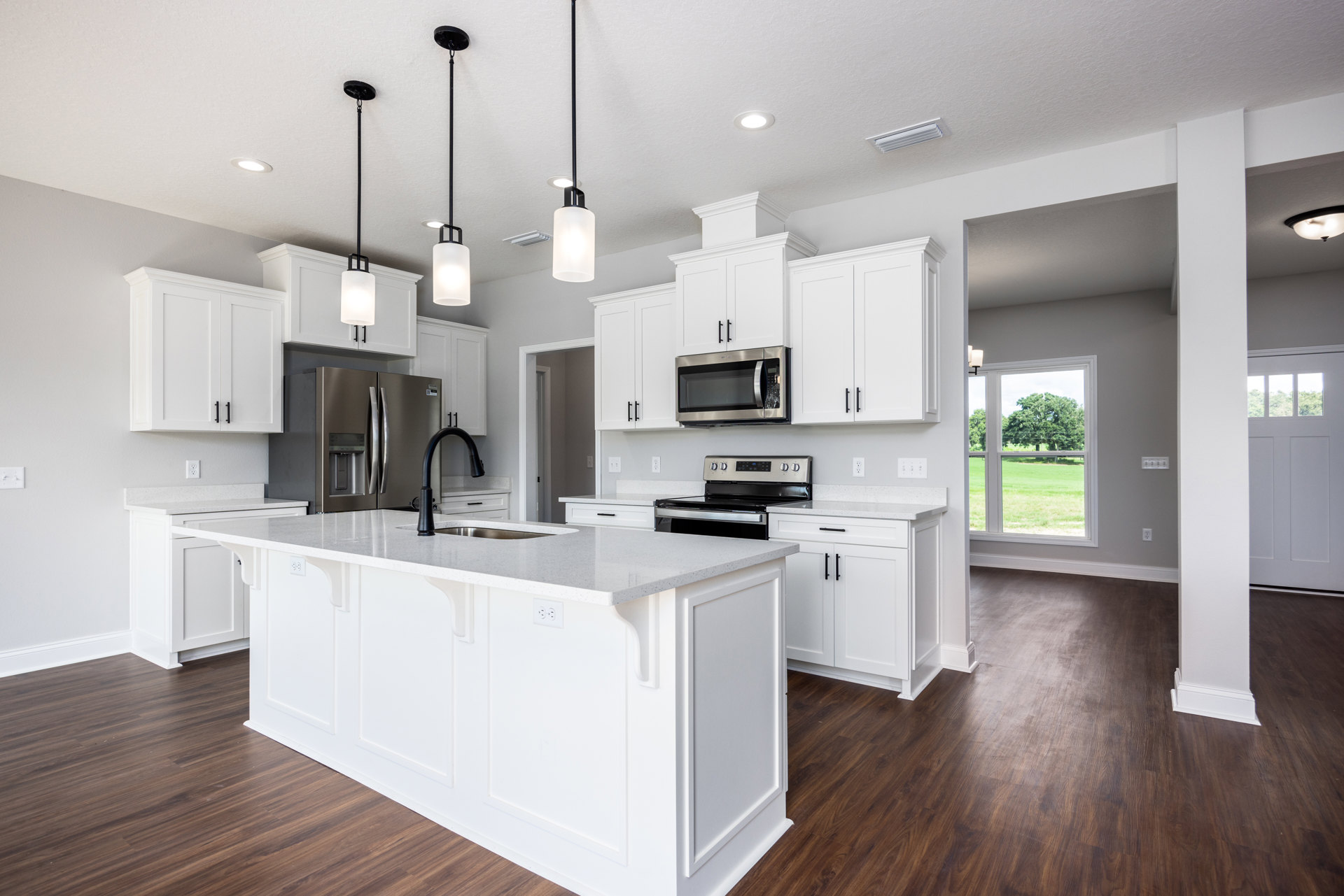 White kitchen with shaker cabinets, stainless steel refrigerator with water dispenser, built-in microwave, wood plank flooring, black pendant lamp, white ceiling molding, and