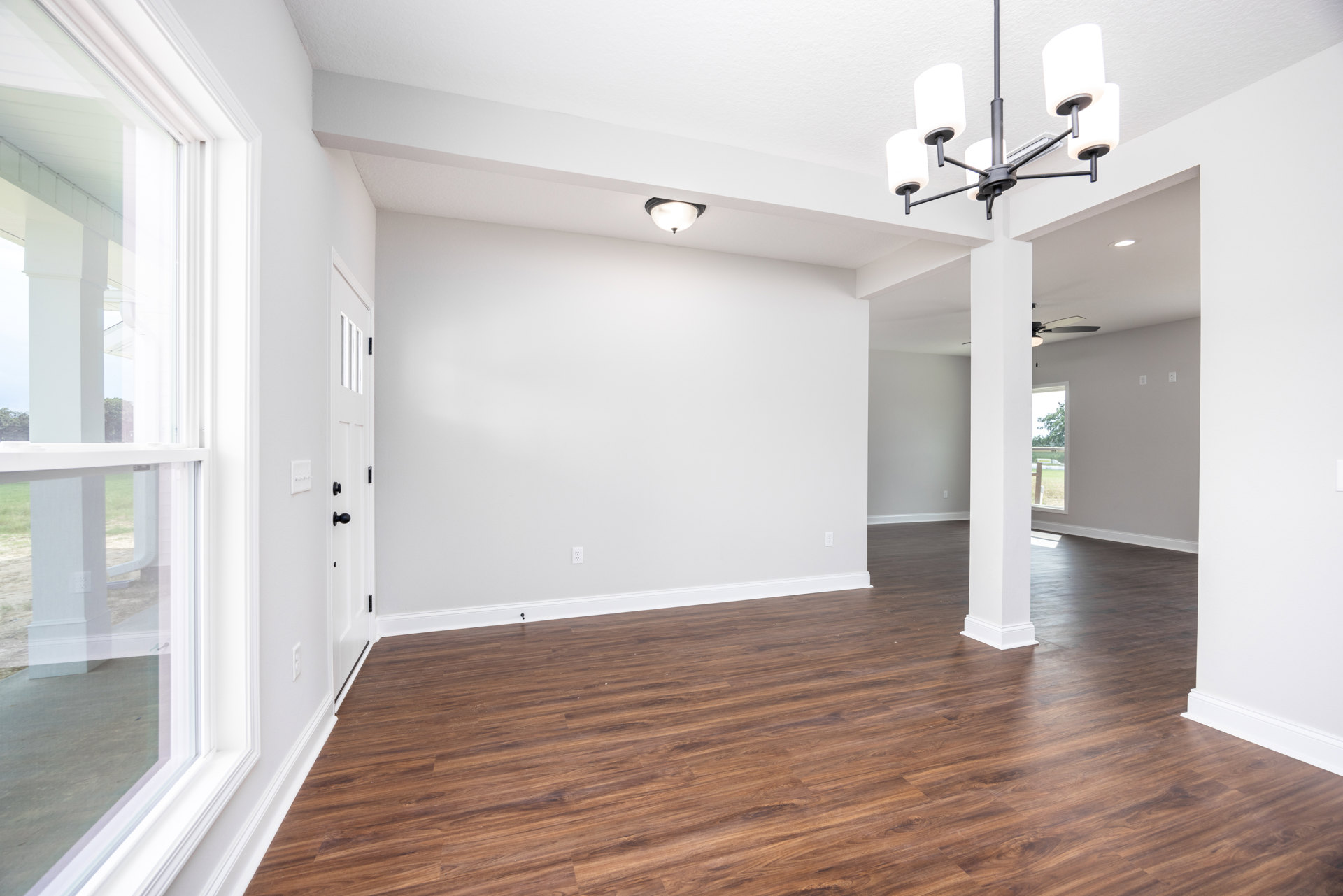 Hardwood floor in a room with white walls and a chandelier featuring white lampshades