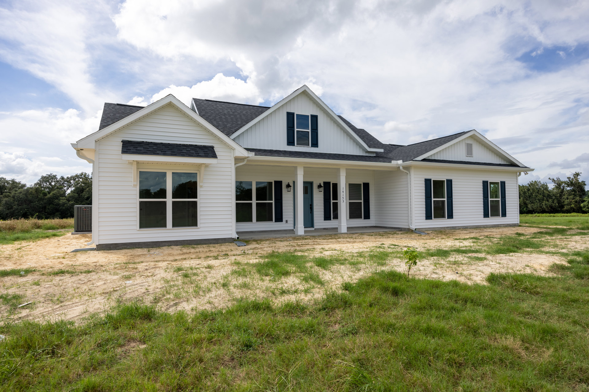 White house with black roof, blue door, white-framed windows, grassy front yard, and tree visible outside window