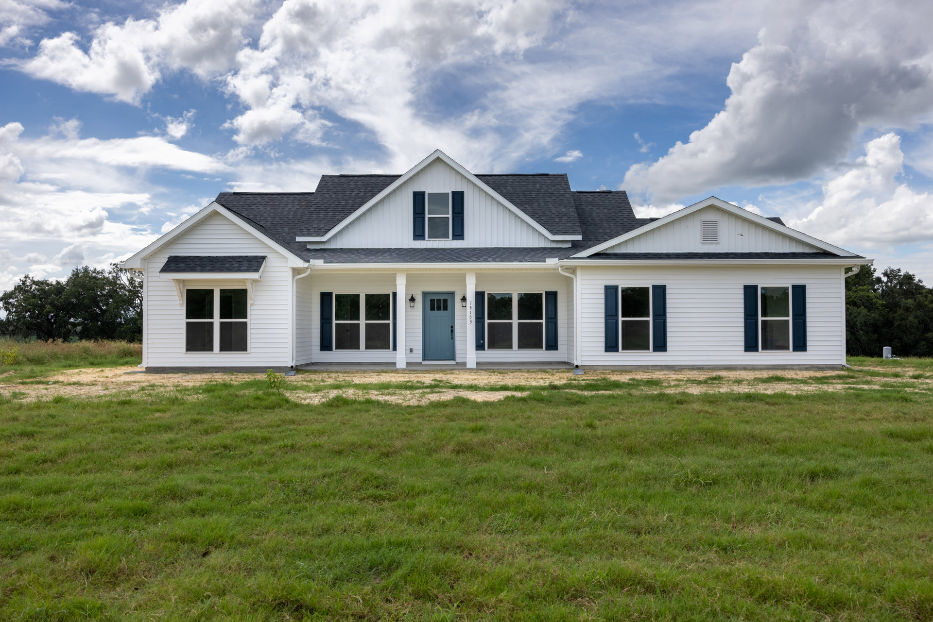 White siding exterior with blue front door, black handle, white-framed windows, gabled roof, and green grass lawn under partly cloudy sky