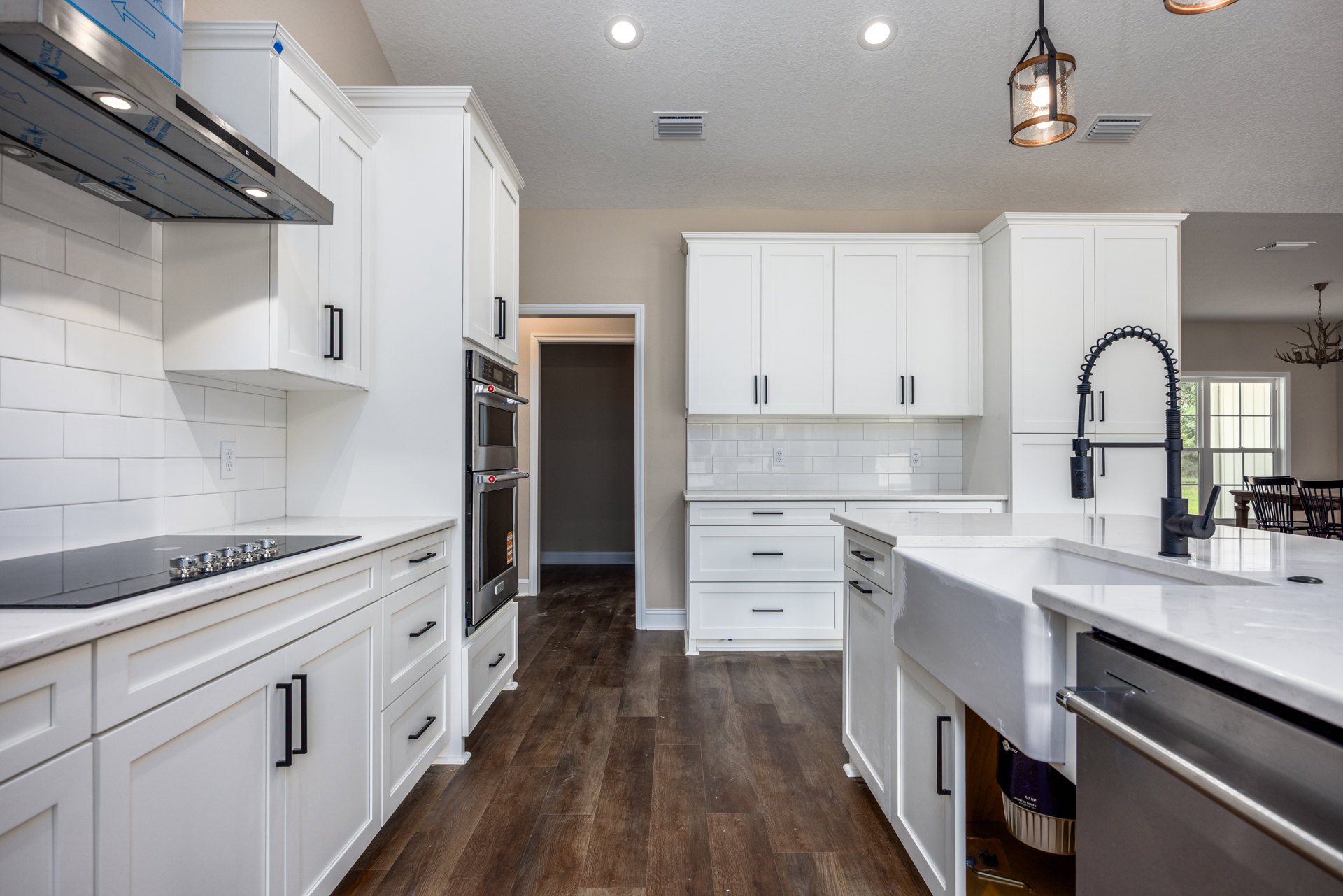 White kitchen cabinets with black handles, wood flooring, stainless steel oven, glass and wood light fixture, tile backsplash, and ceiling lights