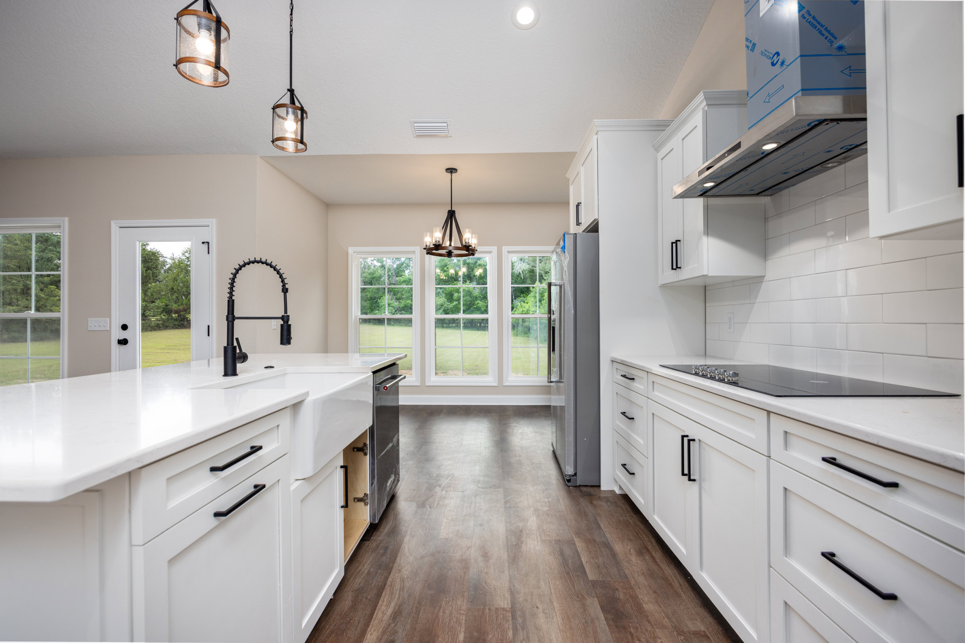 White kitchen cabinets with brushed metal hardware, wood plank flooring, marble countertops, stainless steel sink and faucet, glass pendant lights, black metal pipe detail, and a