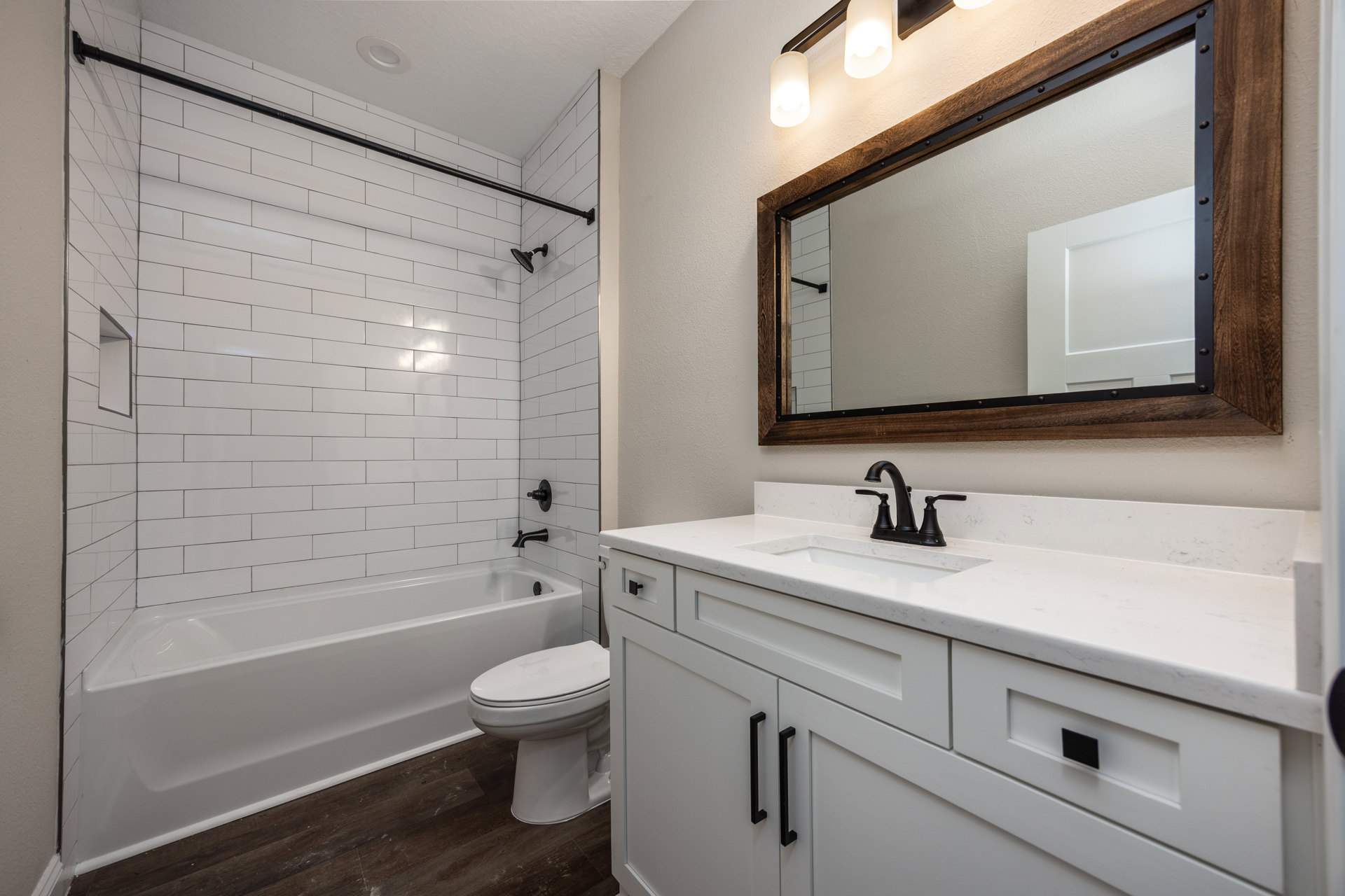 White tile bathroom featuring a wall-mounted mirror above a countertop, freestanding white bathtub beside a closed-lid toilet, chrome fixtures, and neutral finishes.