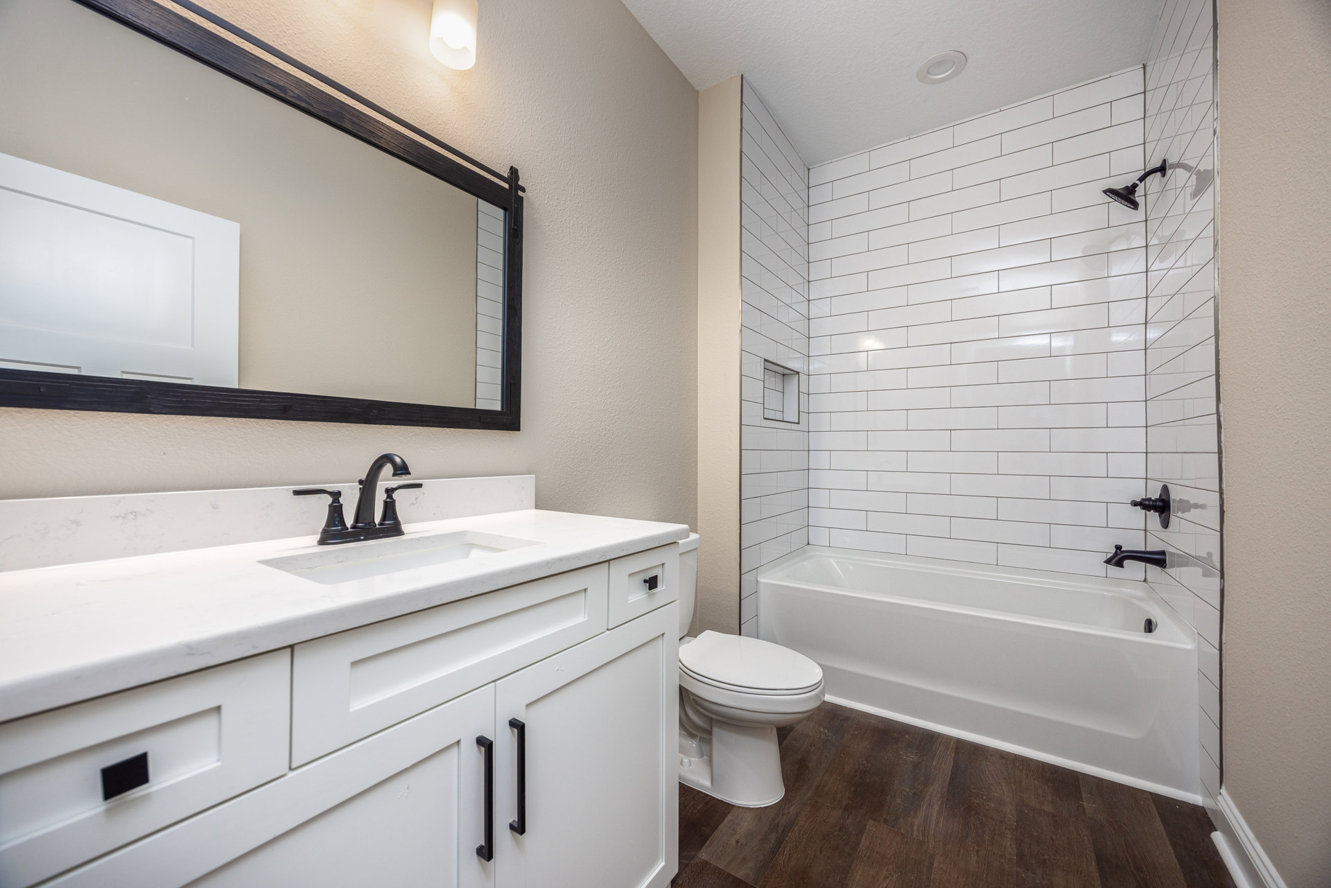 White bathroom with tile walls, freestanding bathtub, white sink on black faucet countertop, and closed toilet seat